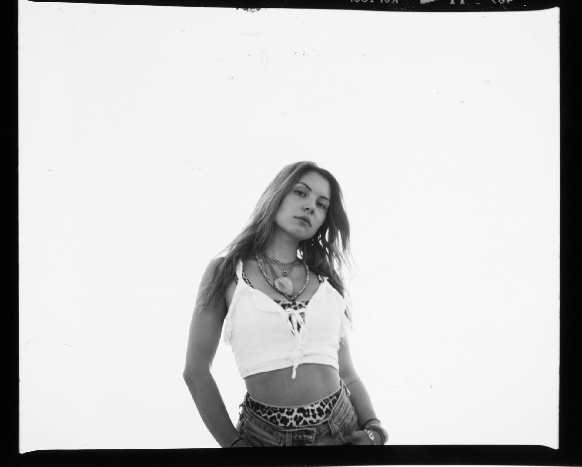 Jeune femme posant en maillot blanc avec bijoux et vêtements à motifs léopard, regardant vers l'appareil, en noir et blanc.
