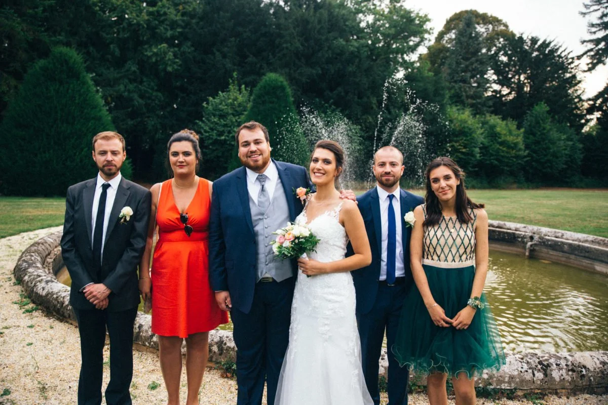 Groupe de six personnes en tenue élégante, posant devant une fontaine dans un parc lors d'un mariage