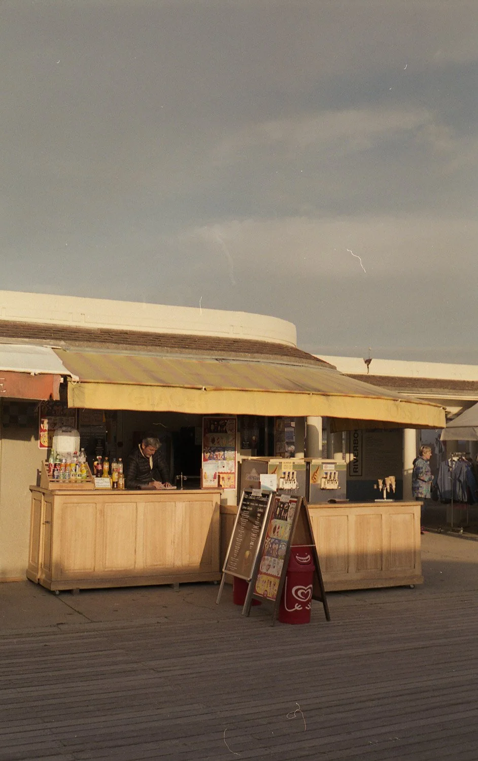 kiosk de vente de boissons et de snacks en plein air avec deux personnes et un panneau de menu