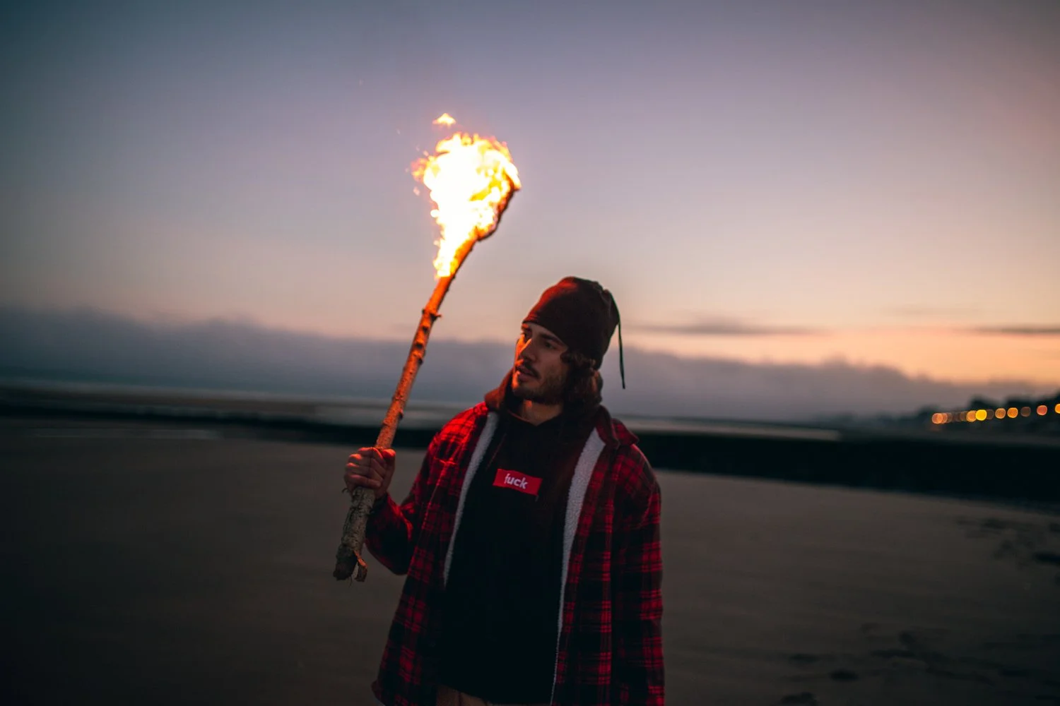 Jeune homme tenant une torche en feu sur la plage au coucher du soleil.