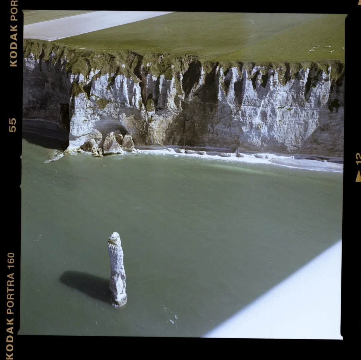 Falaises blanches côtières avec un promontoire rocheux dans une mer verdâtre et un champ vert en haut de la falaise.