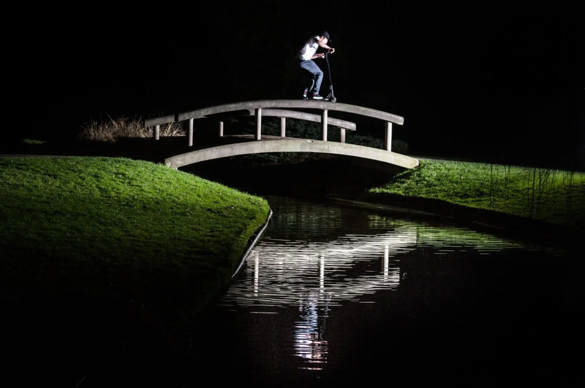 Person sur un scooter sur un pont en bois la nuit, reflet dans l'eau