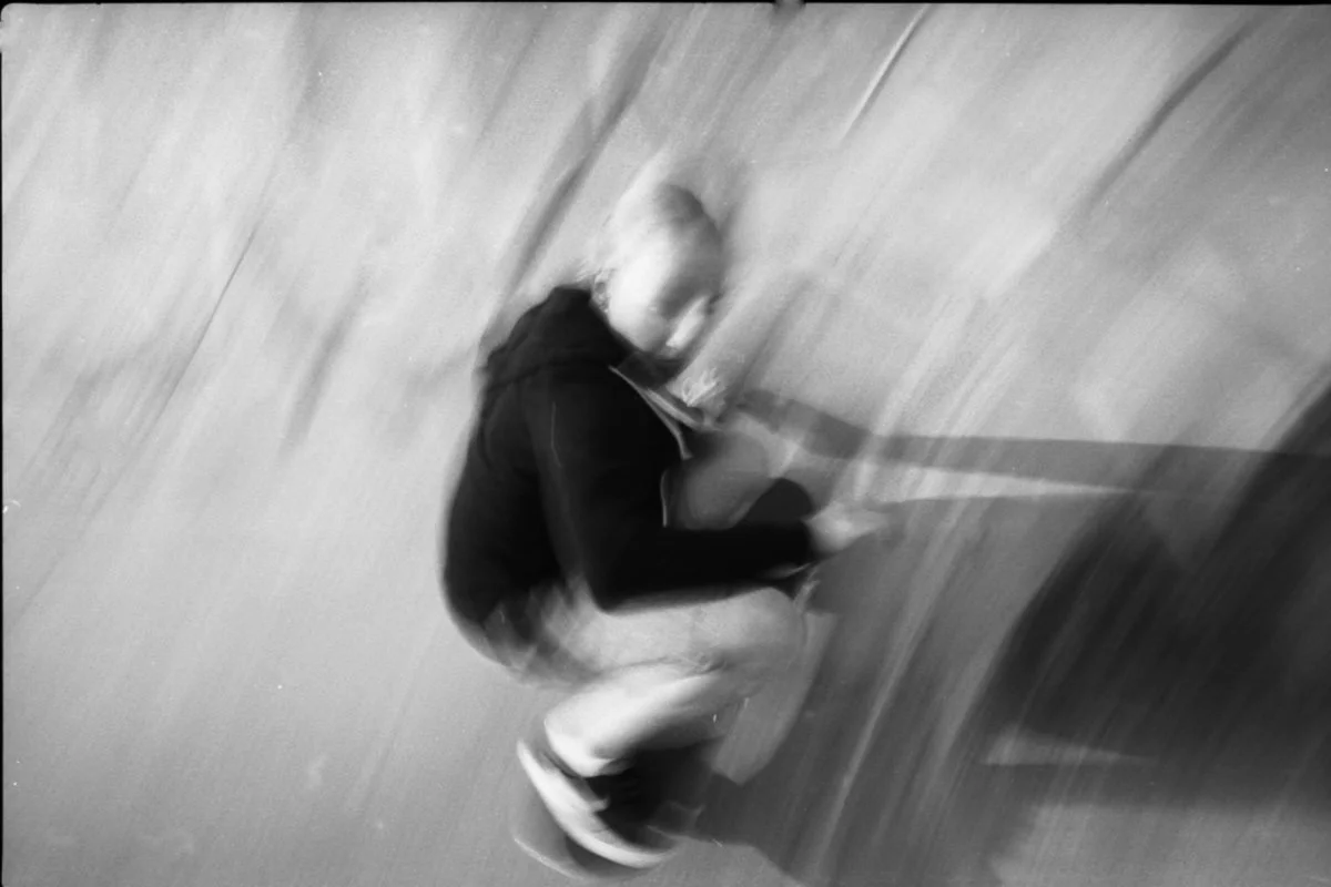 Jeune garçon blond assis par terre, regardant un téléphone portable, en mouvement, dans un environnement urbain.