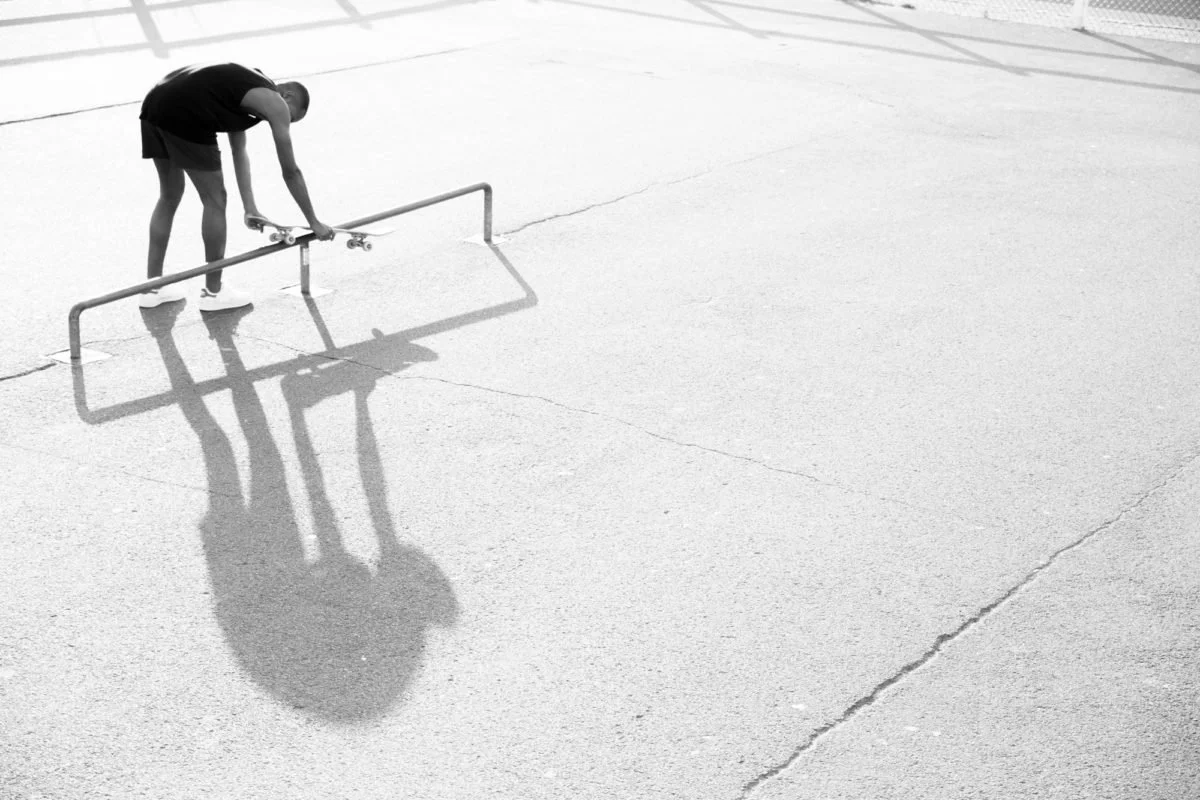 Un garçon fait du skateboard sur un terrain vide à Deauville, il est penché en avant en se préparant à descendre une rampe en métal.