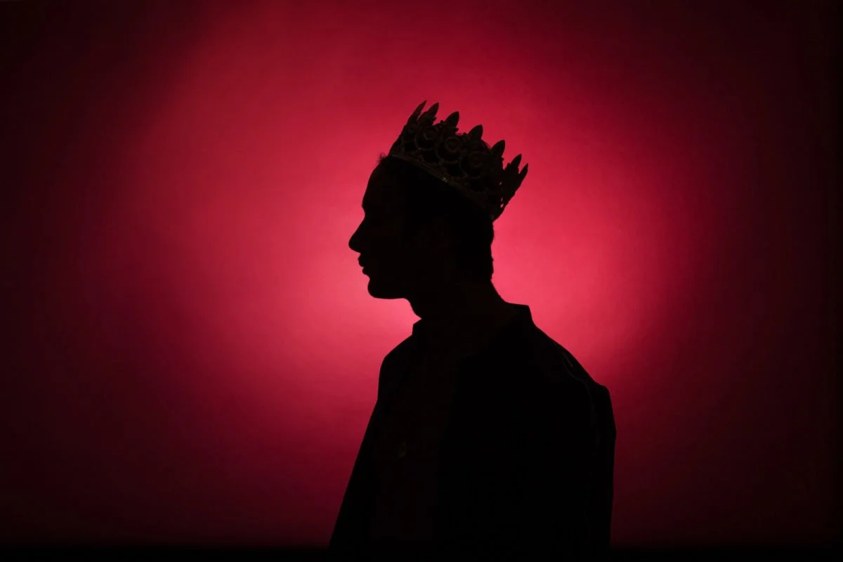 Silhouette d'une personne portant une couronne, avec un fond rouge foncé.