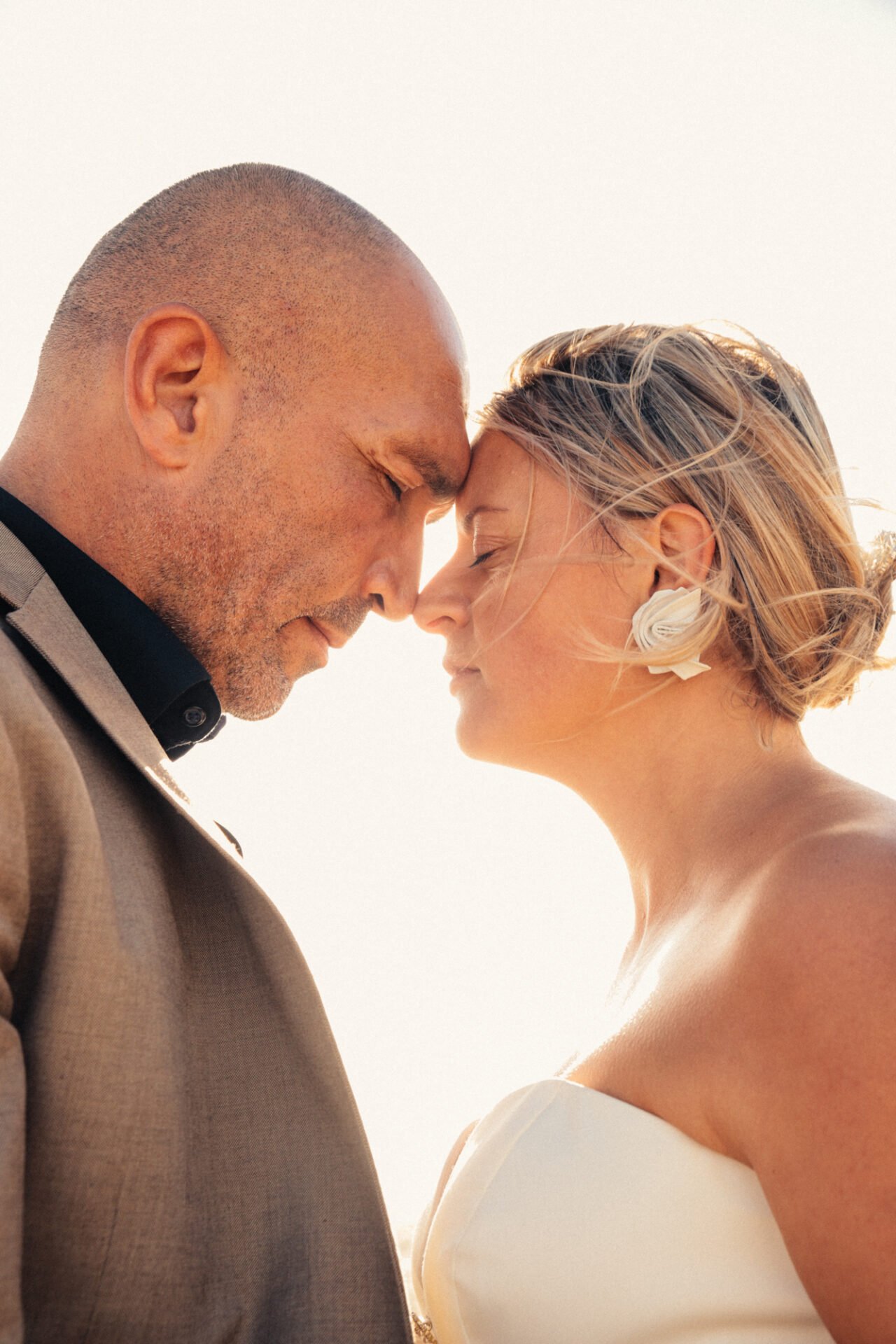 Un couple s'apprête à s'embrasser, avec la tête inclinée en avant, leurs fronts et leurs nez se touchant, sous une lumière douce et chaleureuse.