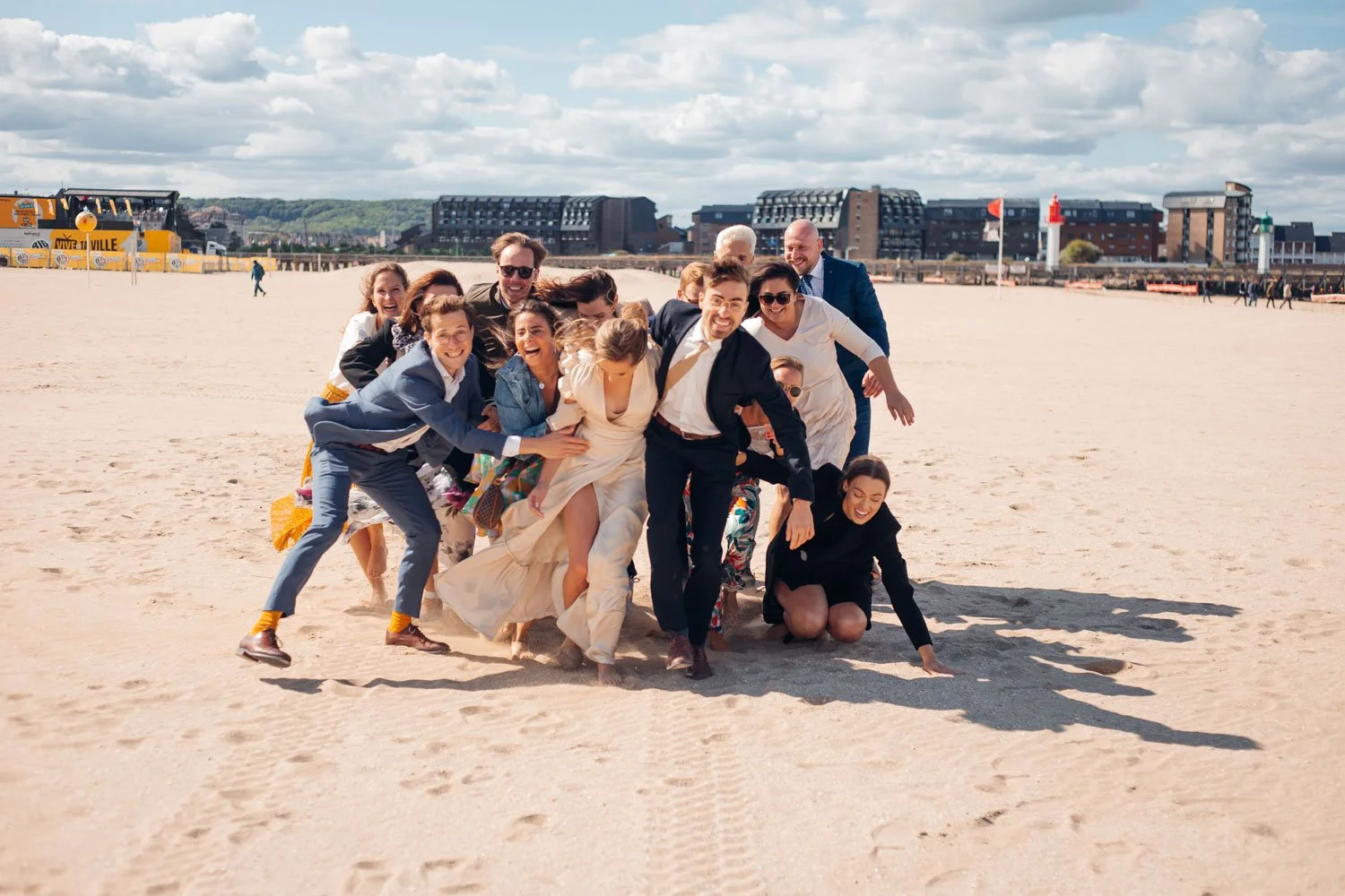 Groupe de personnes en tenue de mariage sur une plage, riant et posant pour une photo.