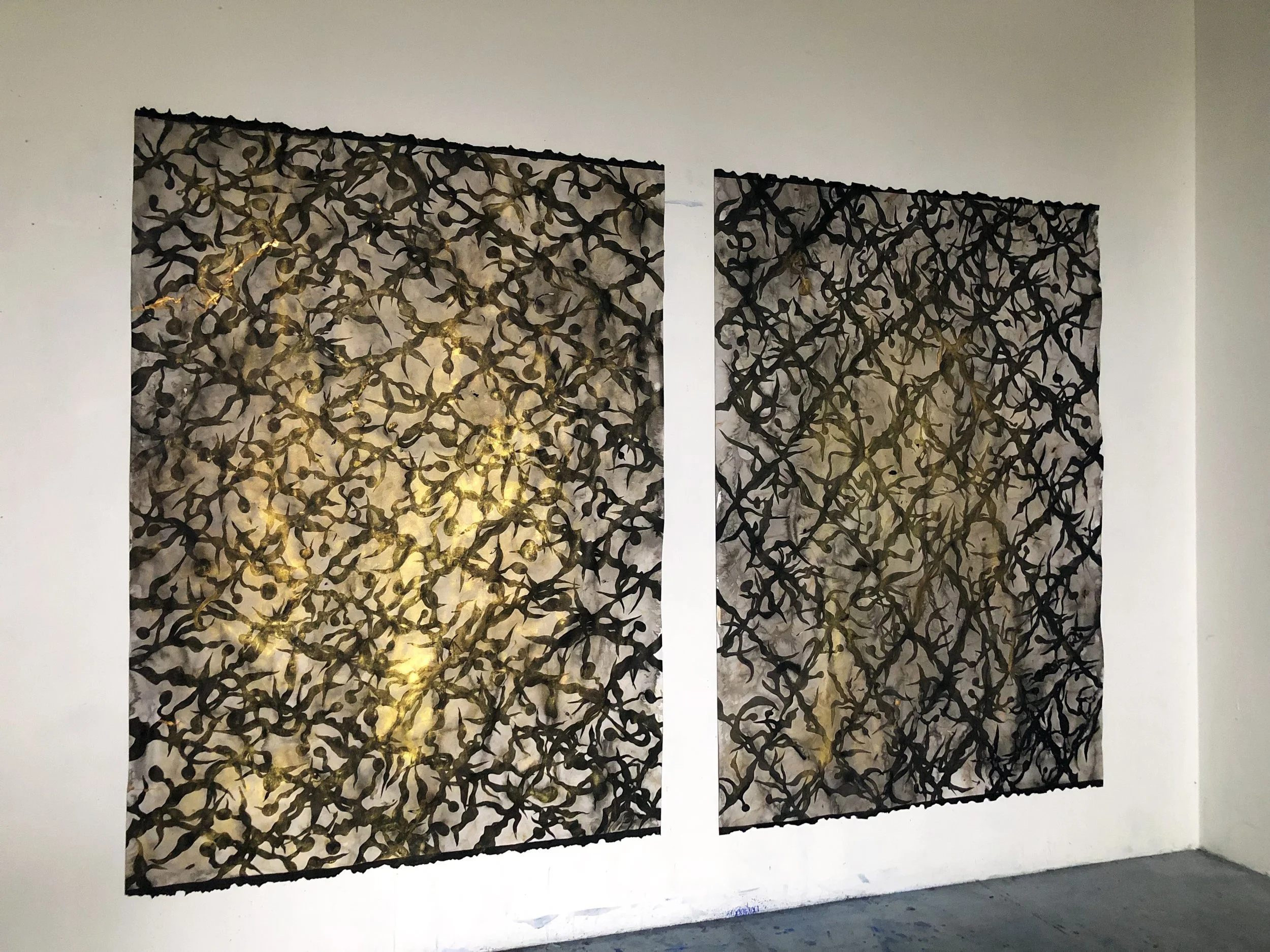 Deux peintures ornementales  avec un motif de grille de sargasses noires et dorées sont accrochées sur un mur blanc.