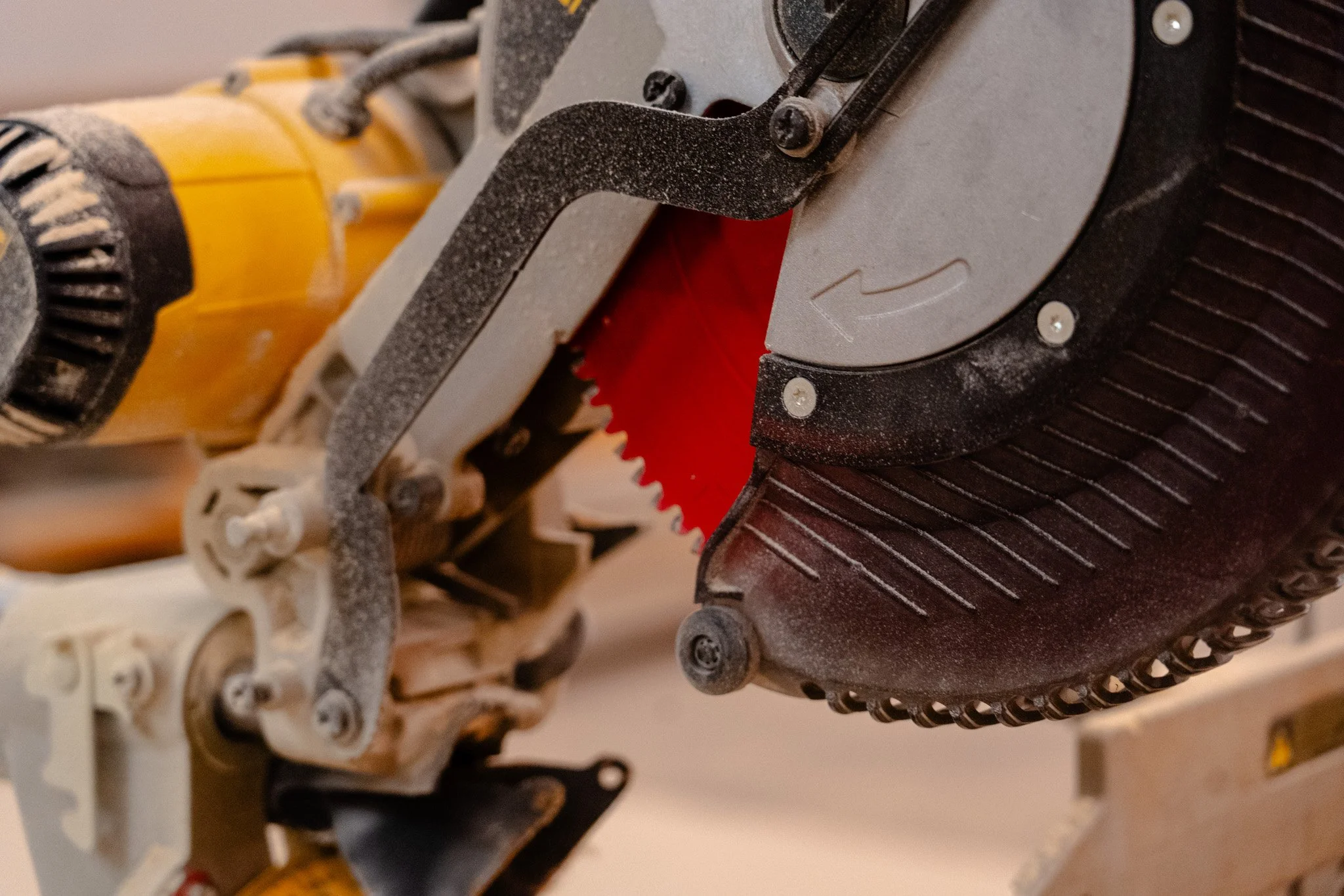 Close-up photo of a miter saw, showing the saw blade, metal fence, and part of the yellow and black power tool. Dust and screws are visible on the saw.