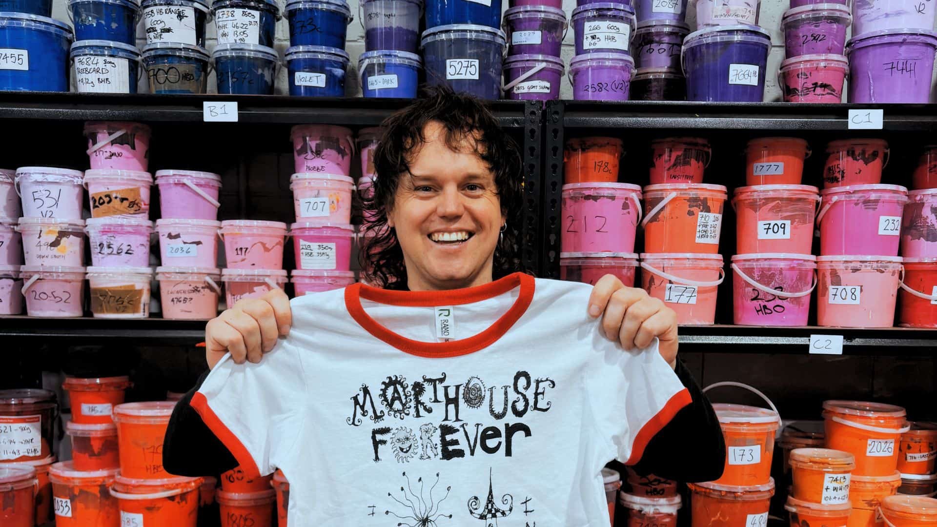 Adam holding a Malthouse Forever printed shirt at Tee It Up.