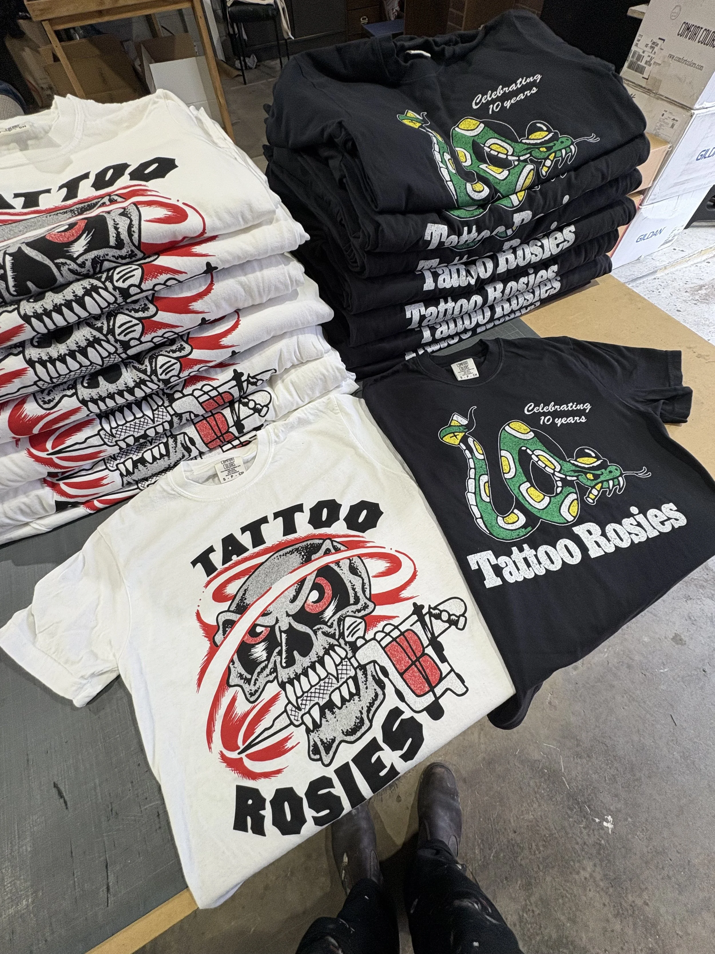 Printed Tattoo Rosies T-shirts laid out with stacks of finished merch.
