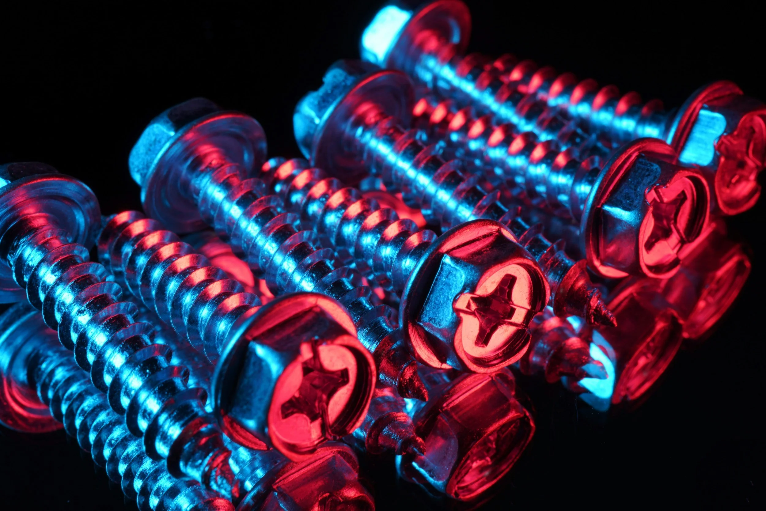 Close-up of metallic screws illuminated with red and blue colored lights against a black background.