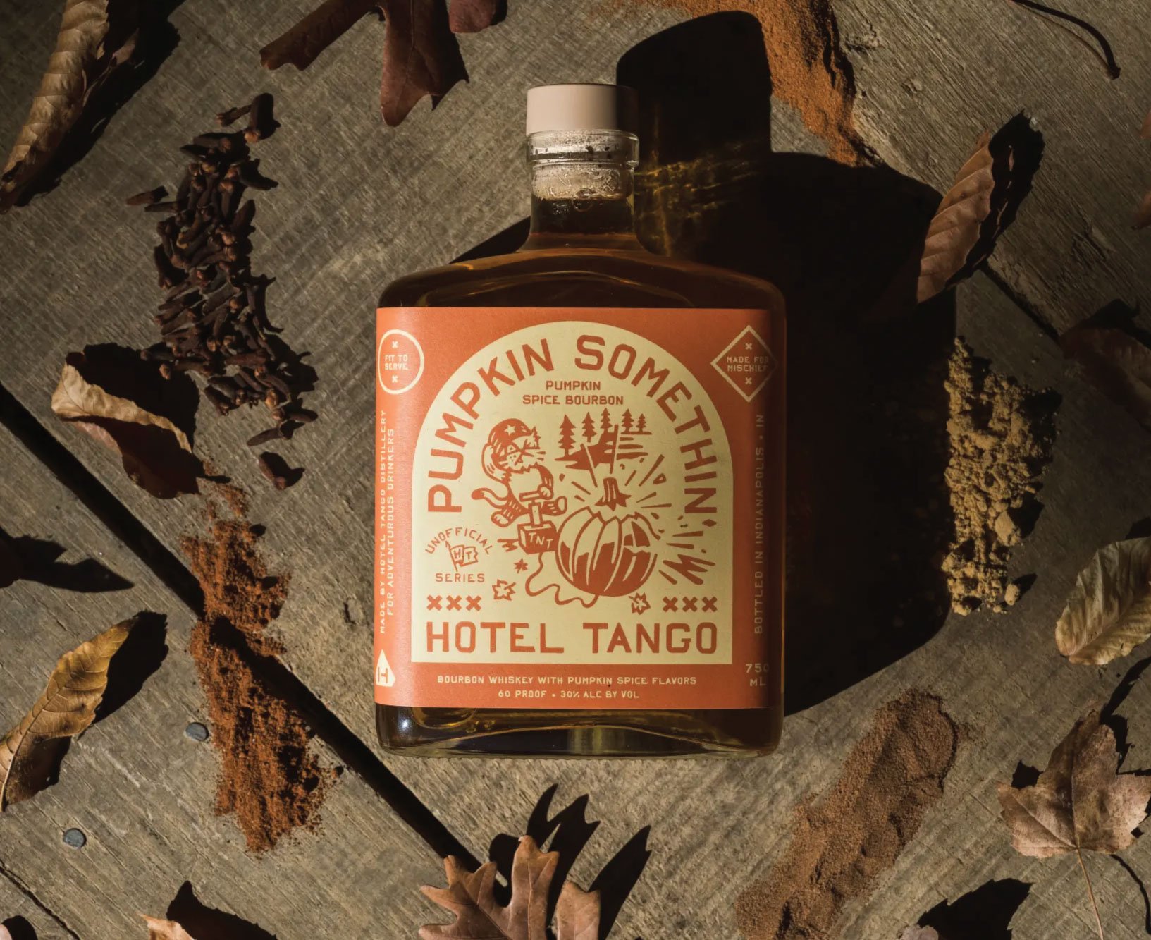 A bottle of Pumpkin Somethin' Whiskey with pumpkin spice flavors, placed on a wooden surface surrounded by dried leaves and spices.