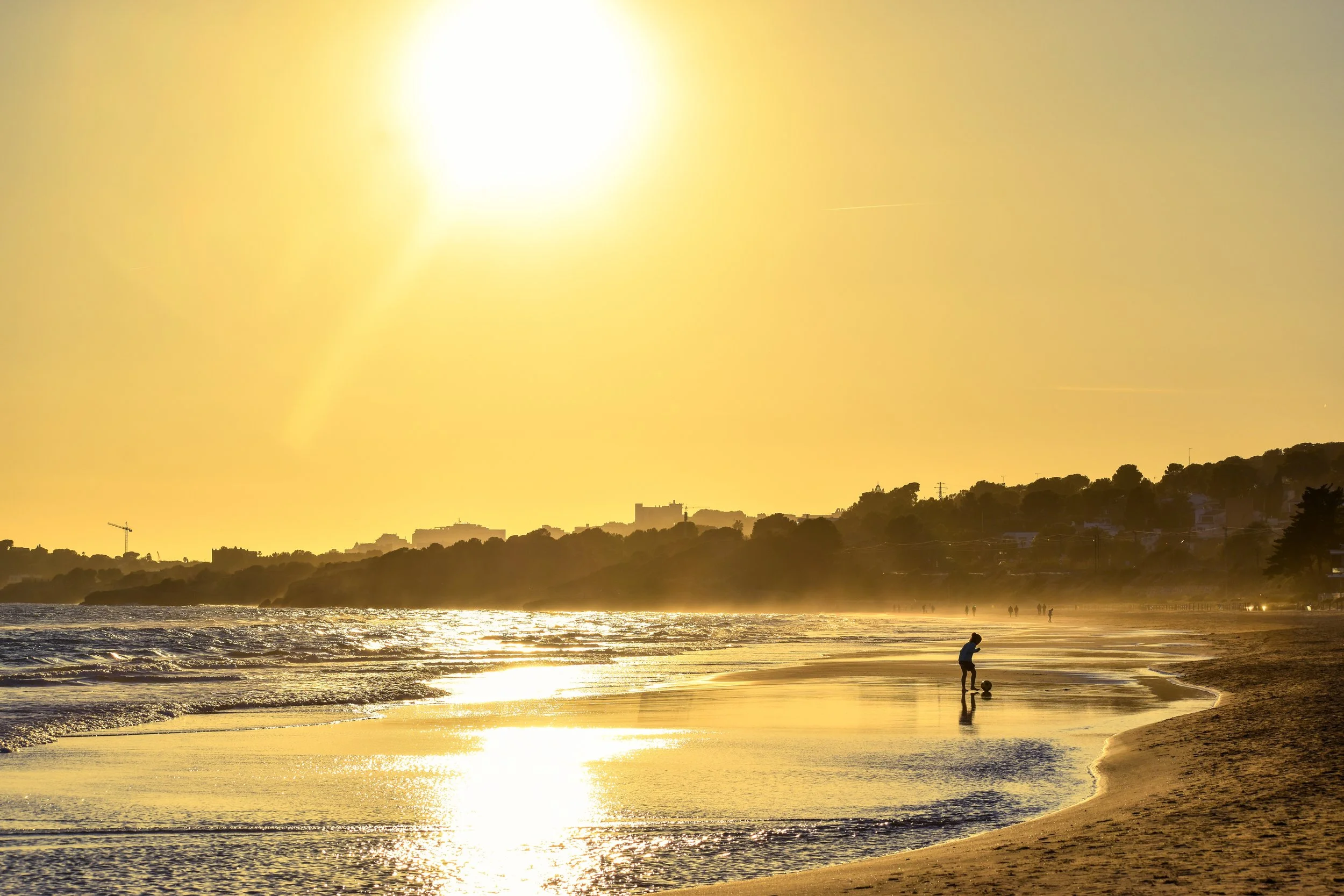 Silhouette of a child playing with a ball on the beach in the golden light before sunset.