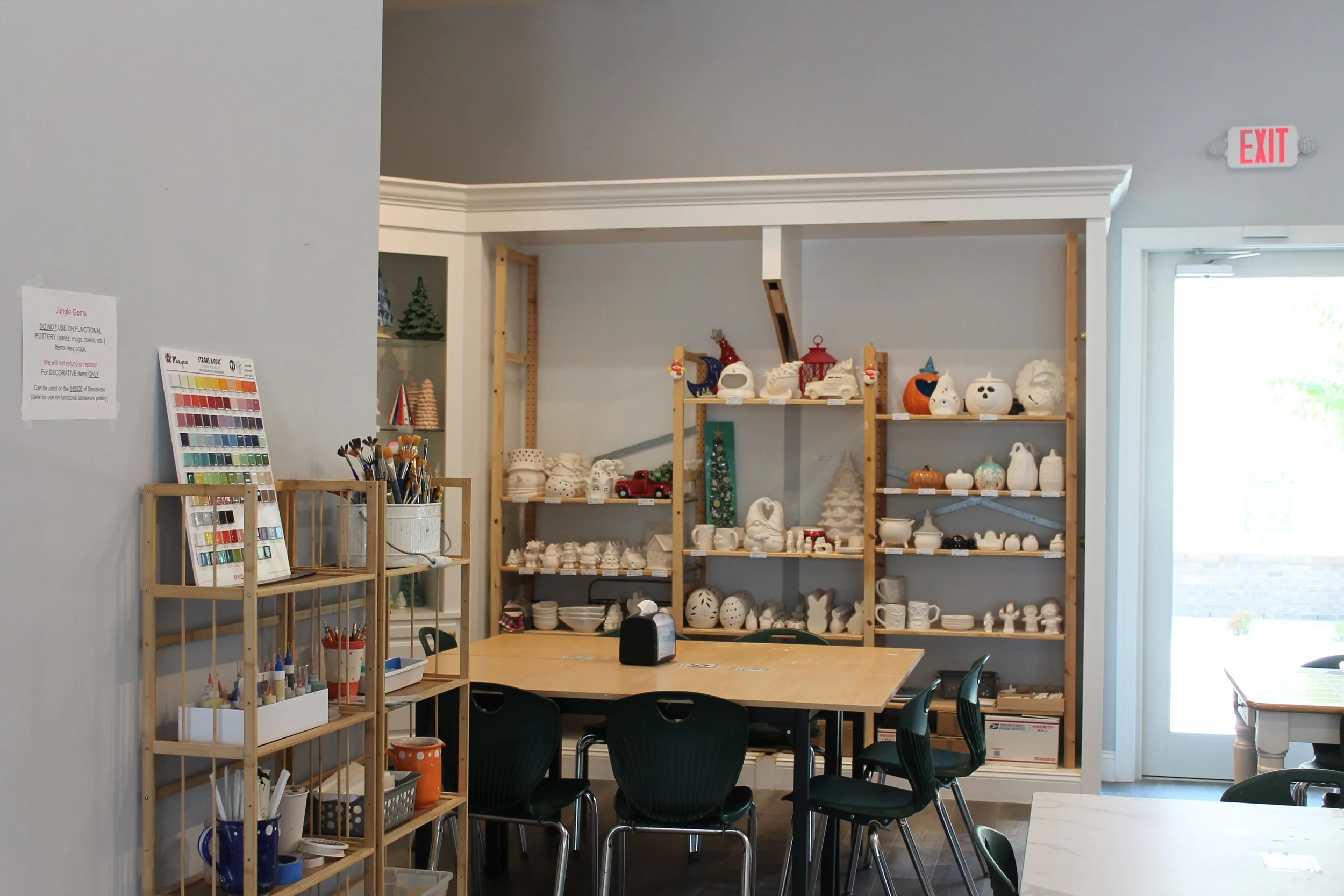Interior of a craft store with shelves filled with ceramic Halloween and holiday decorations, a table with chairs, and a wall painted light gray.