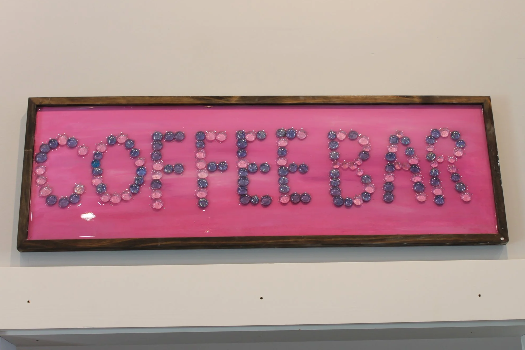 Pink sign with the word 'CYCLE' spelled out with purple and pink round decorative objects inside a wooden frame.