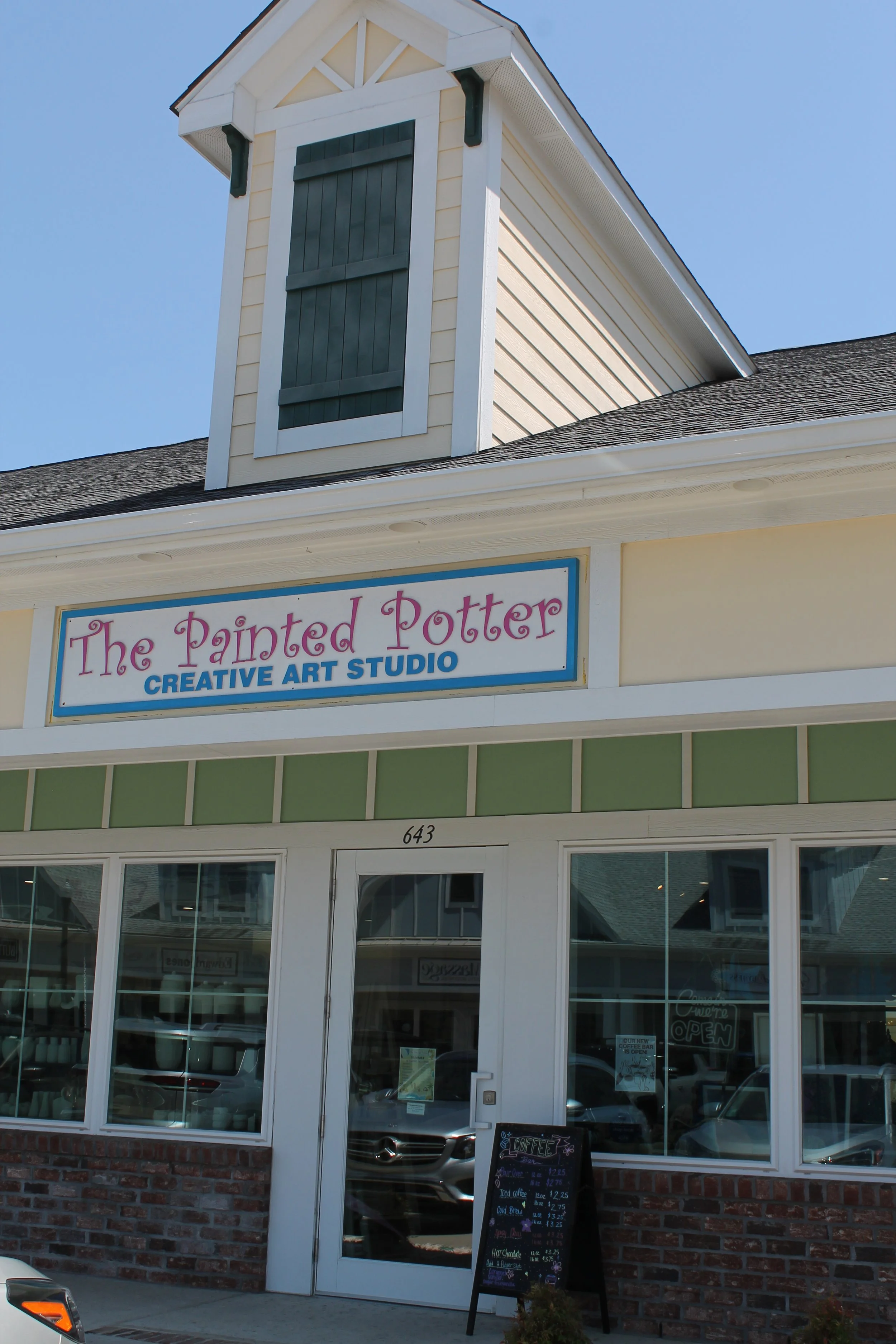 storefront with a sign that reads 'The Painted Potter Creative Art Studio,' large front windows, and a blackboard menu outside offering various coffee beverages.
