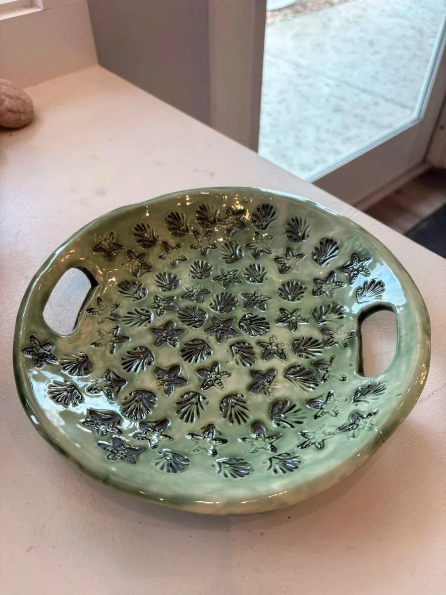 Green ceramic sifter bowl with black shell and starfish patterns on a white countertop near a glass door.