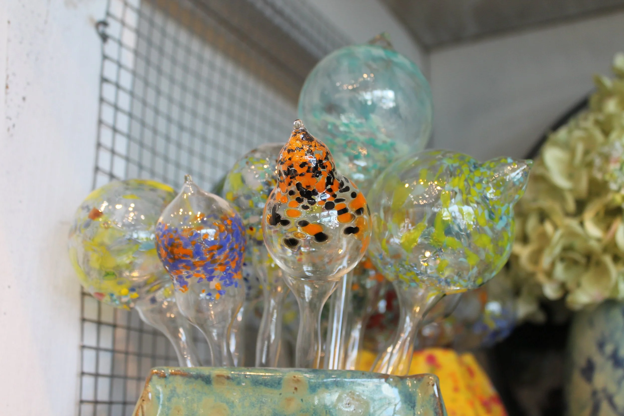 Colorful hand-blown glassart glass pieces with speckled patterns on display on a wire rack.