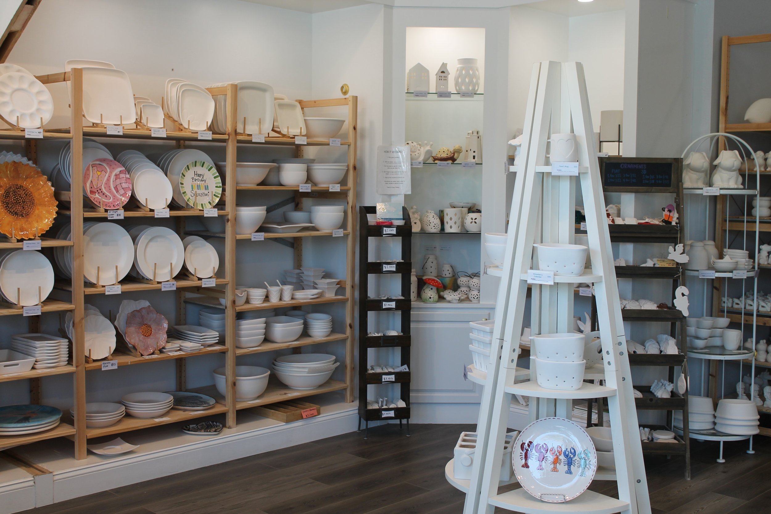 A store display of white ceramics, including plates, bowls, and decorative items, arranged on wooden shelves and white display stands.