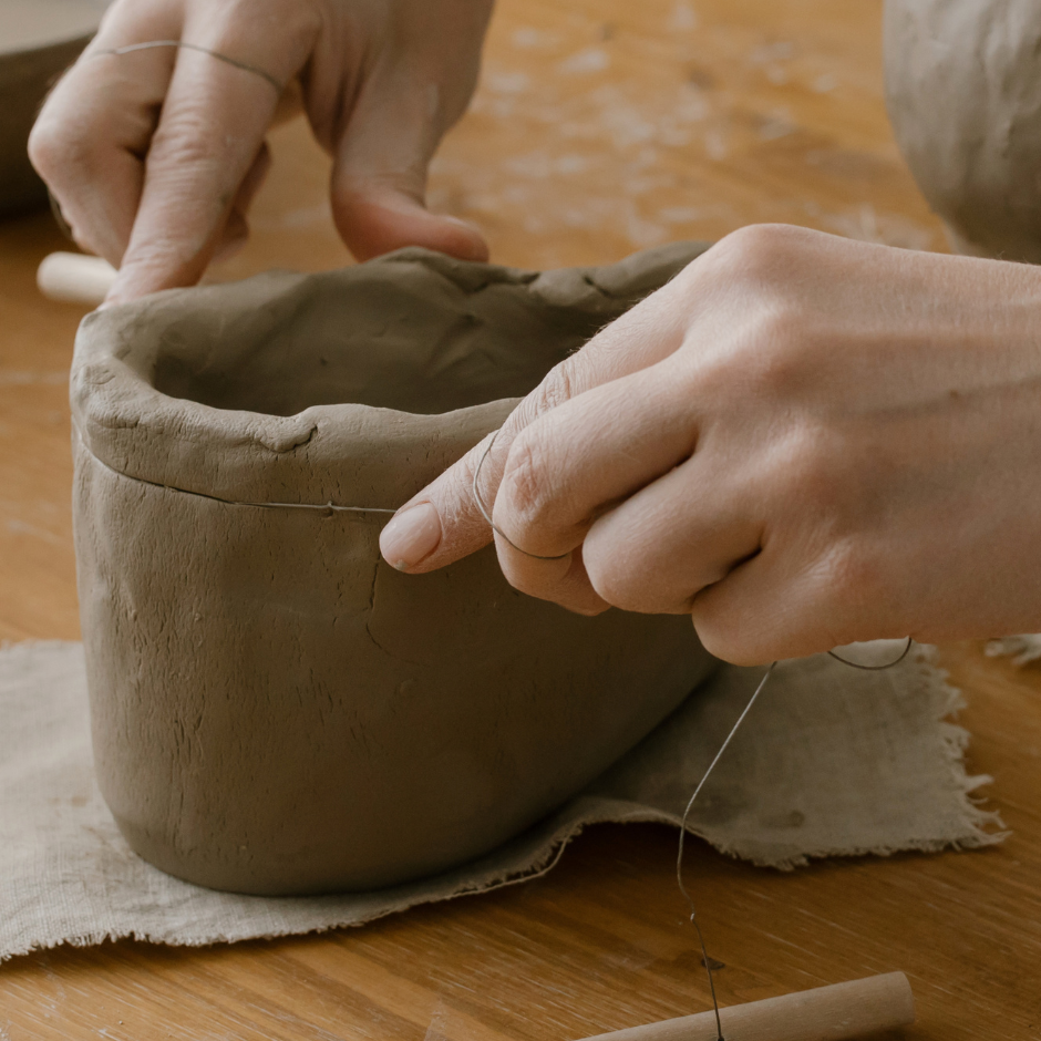 Hands shaping a clay vessel on a wooden table
