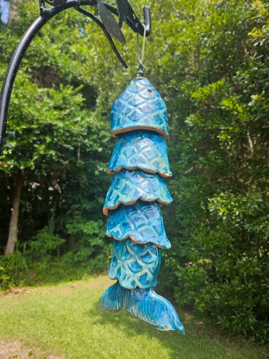 Blue ceramic fish wind chime hanging outdoors in a garden.