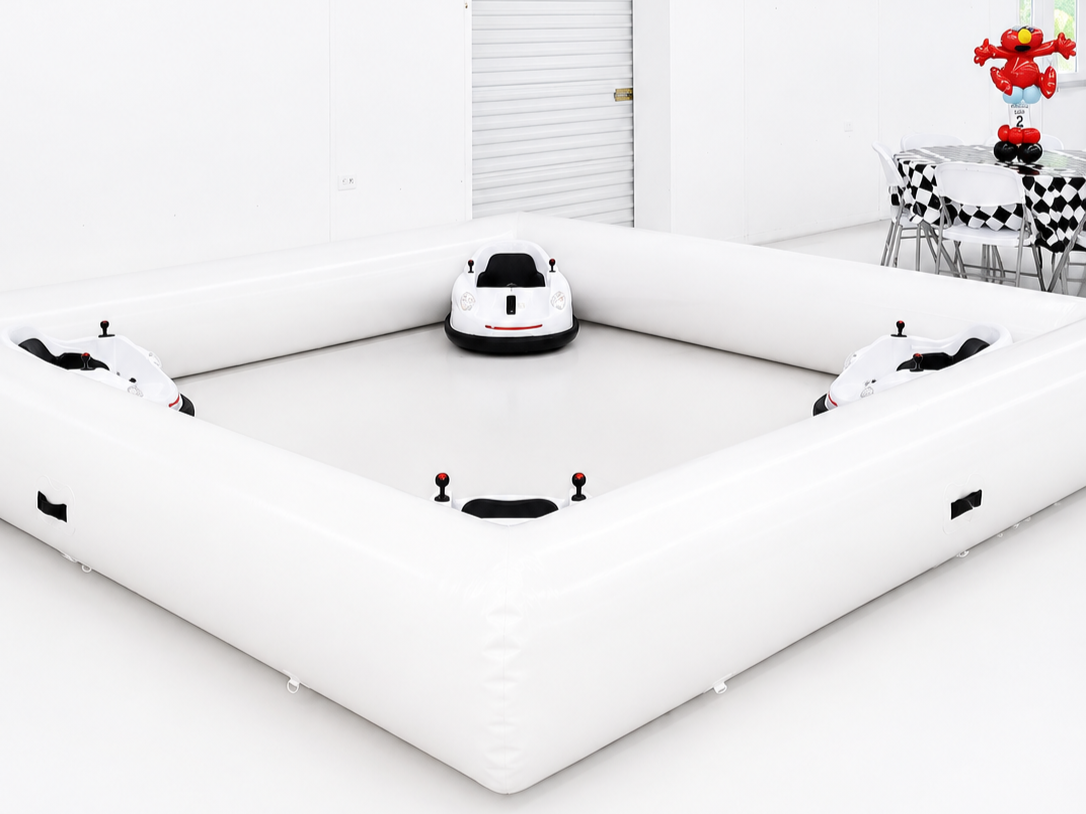 Inflatable ball pit with robotic cars, a table with black and white checkered tablecloth, and a red balloon sculpture in the shape of a flower.