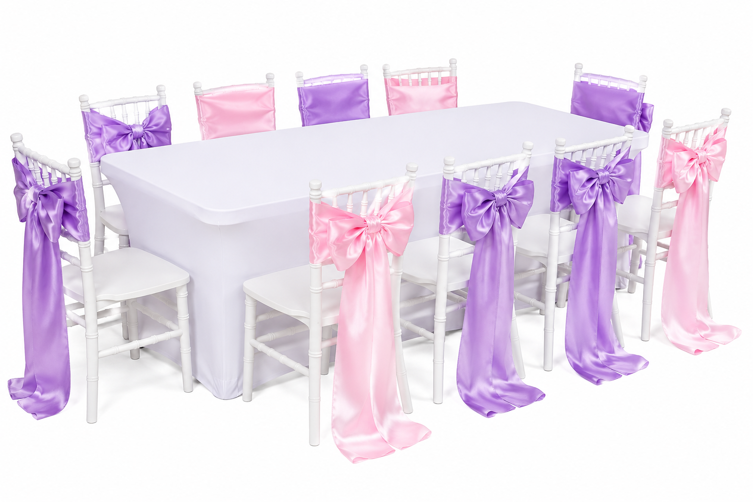 A large rectangular table covered with a white tablecloth, surrounded by white chairs decorated with purple and pink satin bows and sashes, likely set up for a celebration or event.