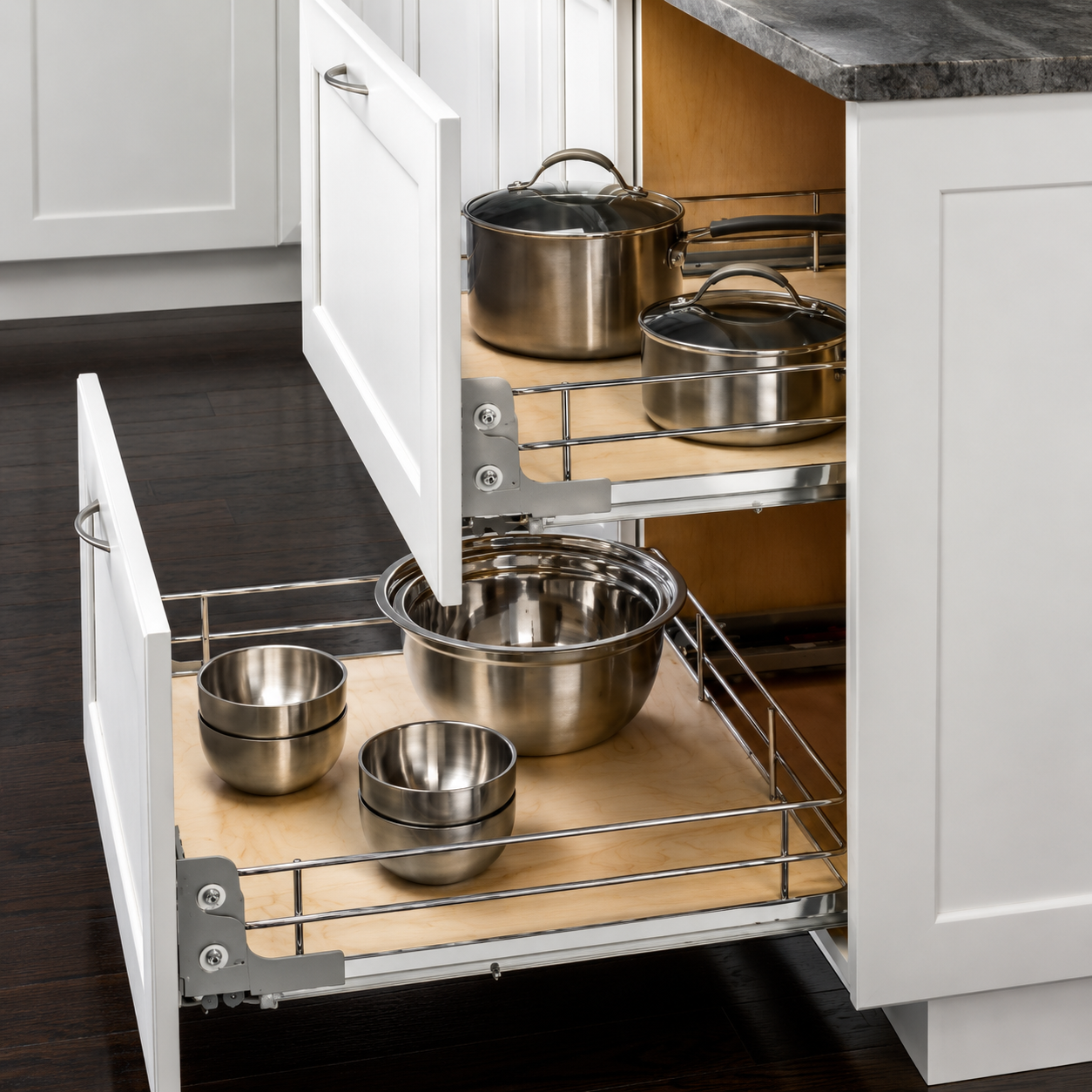 Kitchen cabinet with pull-out shelves containing stainless steel mixing bowls and pots.