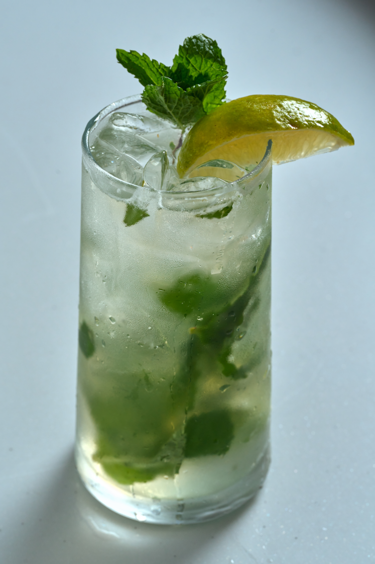 A bright green classic soju mojito in a clear glass with mint leaves and a lime wedge, styled on a clean, neutral backdrop.