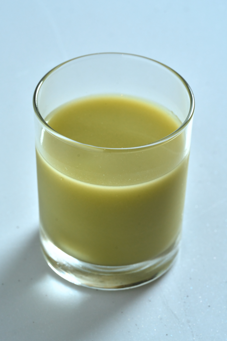 A smooth, green matcha makgeolli served in a clear glass against a light, minimal background.