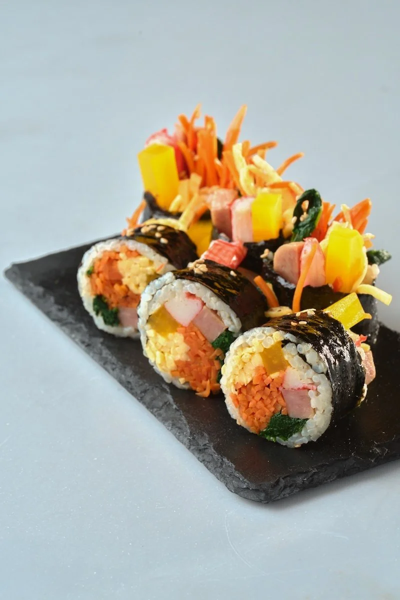 Assorted sushi rolls on a black slate platter with shredded vegetables on top.
