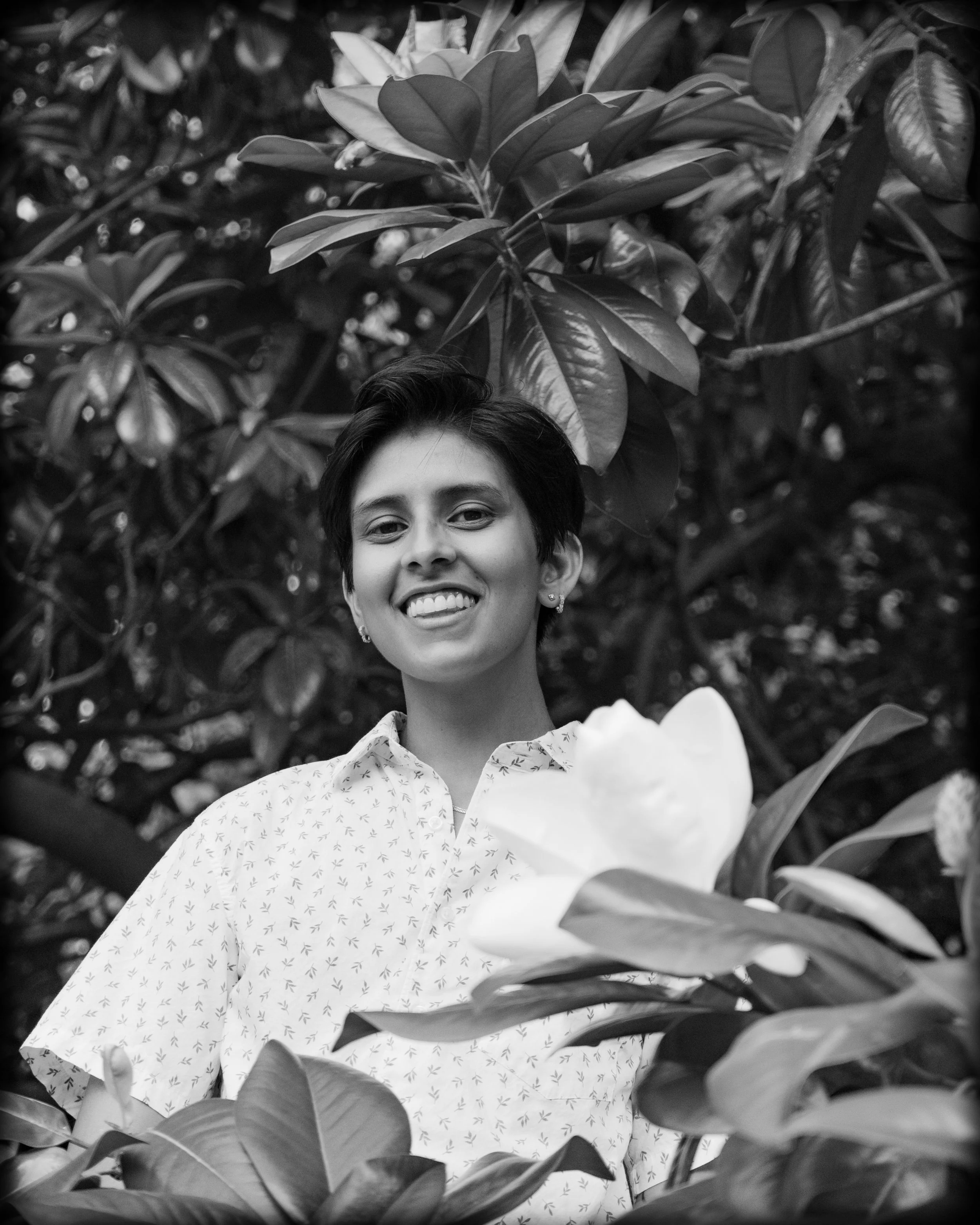 A person with short hair smiling among large leaves and plants, black and white photo.