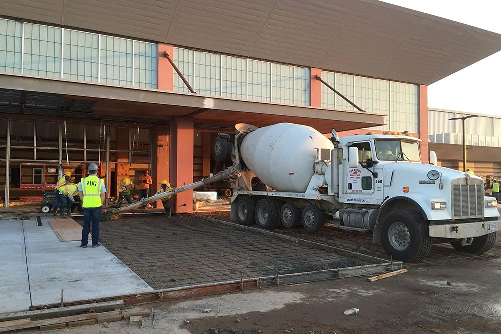 Construction workers in yellow safety vests and helmets working on pouring concrete at a building site with a concrete mixer truck.