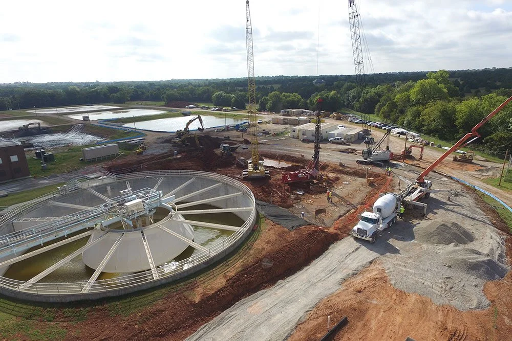 Construction site with cranes, construction vehicles, and a circular water treatment tank.