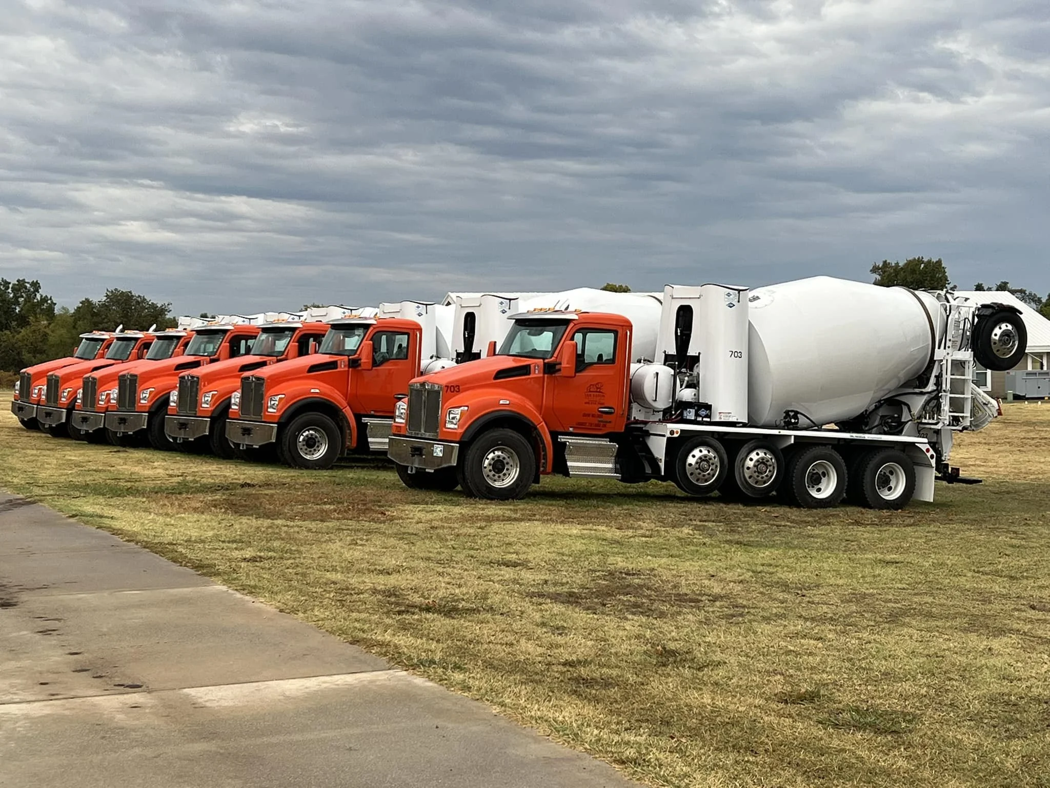 Construction workers pouring concrete at a construction site with a large orange cement truck on a dirt lot.