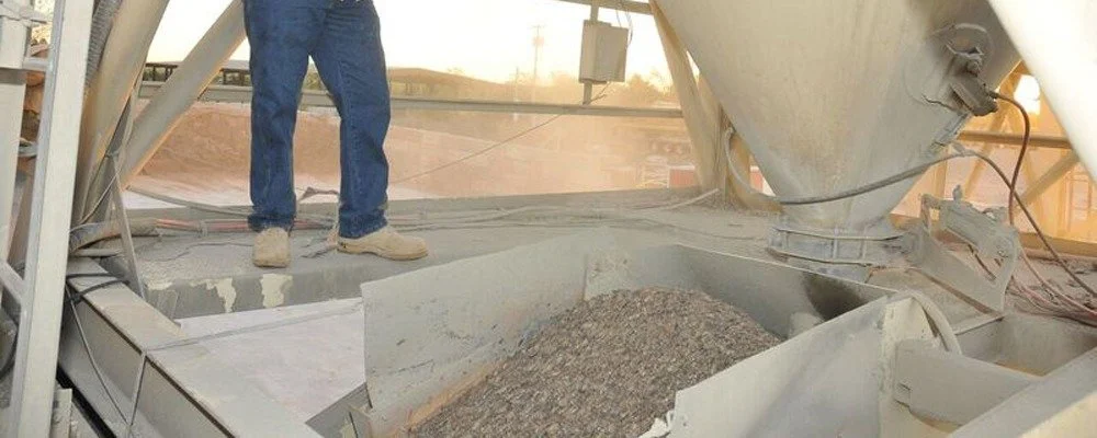 Construction worker standing on concrete surface next to a large cement mixer with gravel inside.