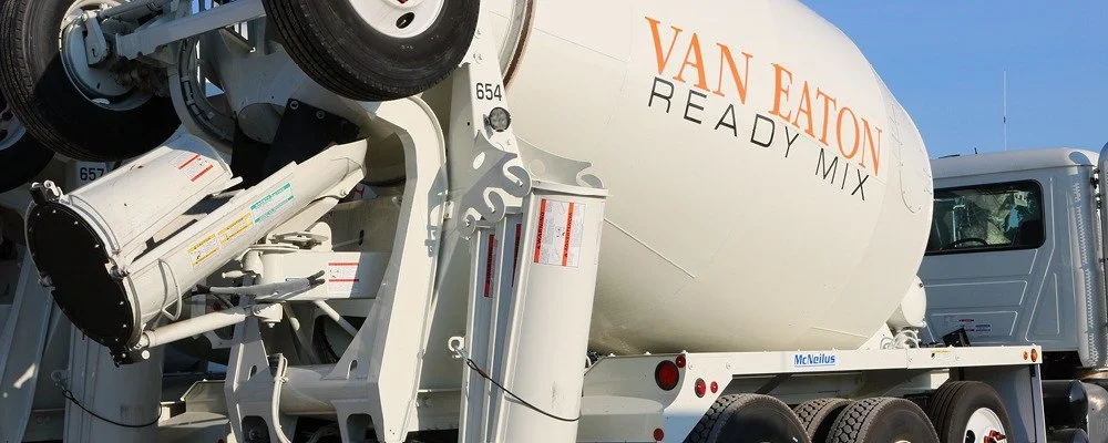 A cement mixer truck with white and gray body, branded with 'VAN EATON READY MIX' on the drum, parked outdoors in daylight.