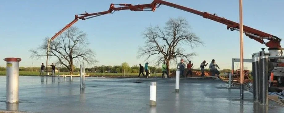 Workers apply a waterproof coating to a flat roof with a large crane and leafless trees in the background.
