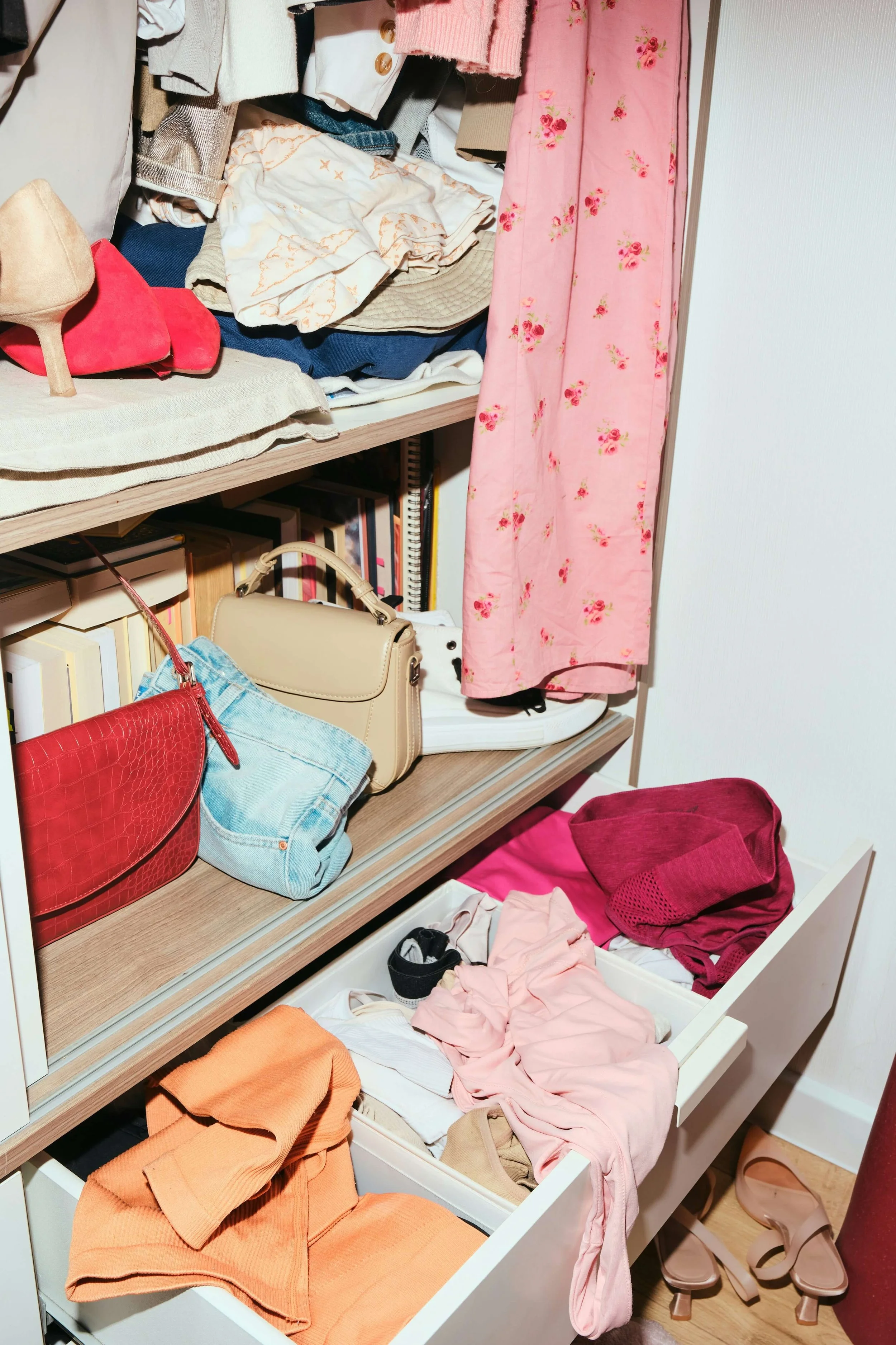 Clothes and accessories inside an open drawer and on shelves, including folded shirts, pants, scarves, handbags, and shoes.
