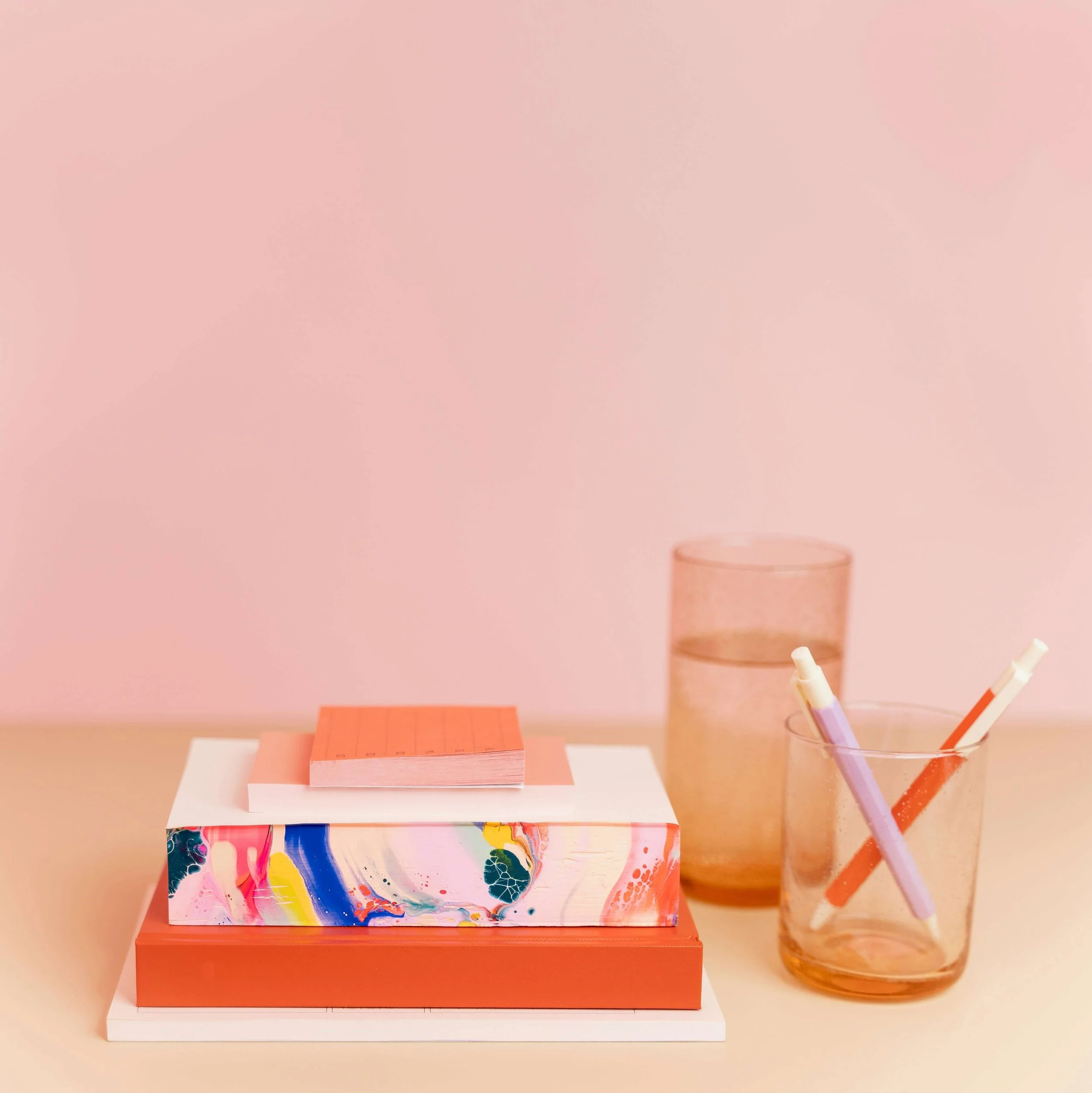 Pink wall with various colorful art supplies and artwork on a desk, including markers, paper, and abstract paintings.