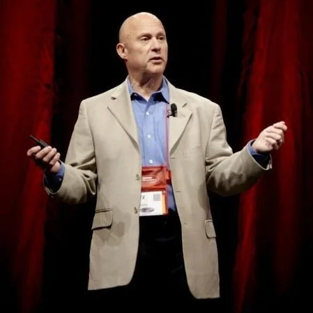 Man giving a presentation on stage with red curtains in the background