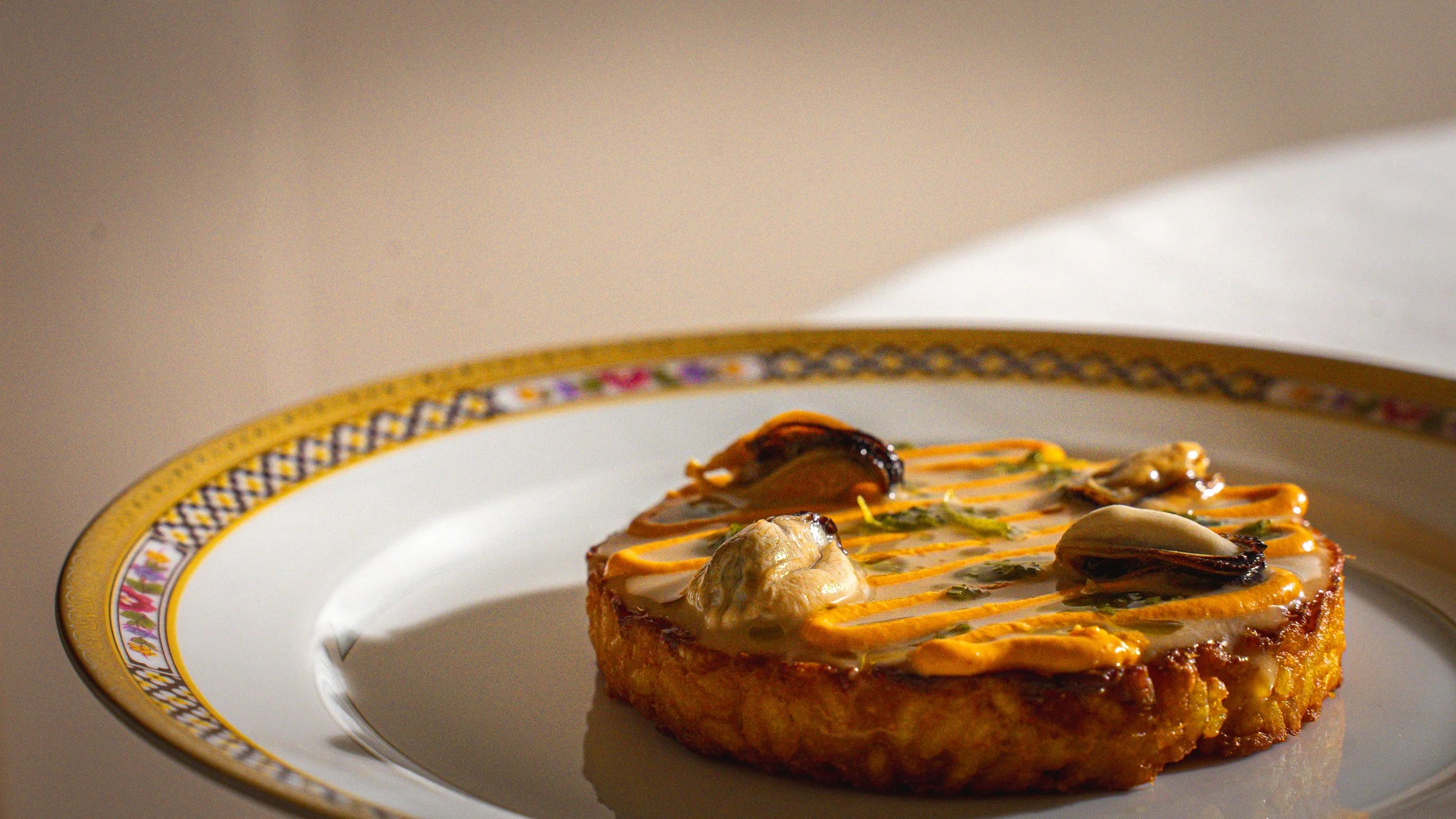 Torta salata decorata con crema arancione, ostriche e altre guarnizioni, su piatto decorato con bordo dorato e motivi floreali.