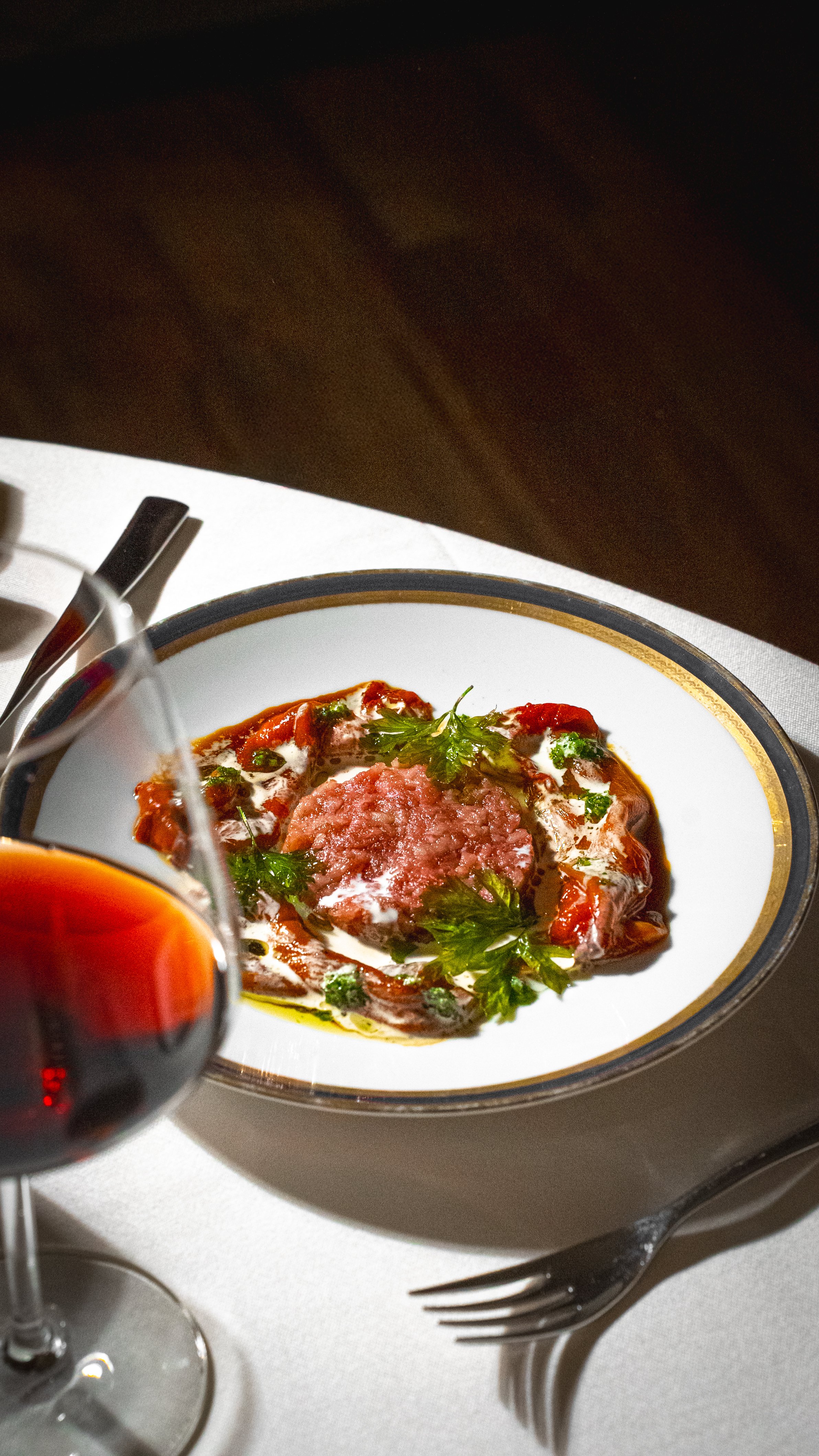 Piatti di carne con sugo di pomodoro, panna e prezzemolo, accompagnati da un bicchiere di vino rosso.