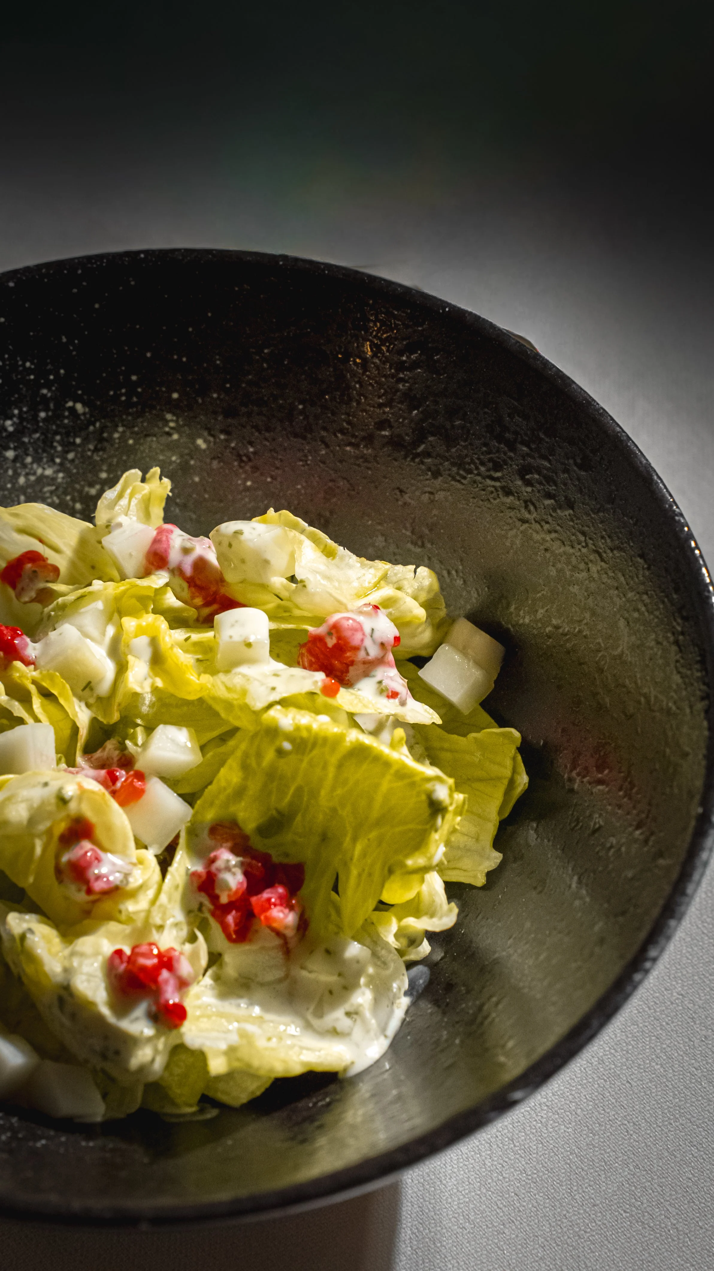 Insalata in una ciotola di ceramica con lattuga, cubetti di formaggio, pomodori rossi e una salsa bianca.