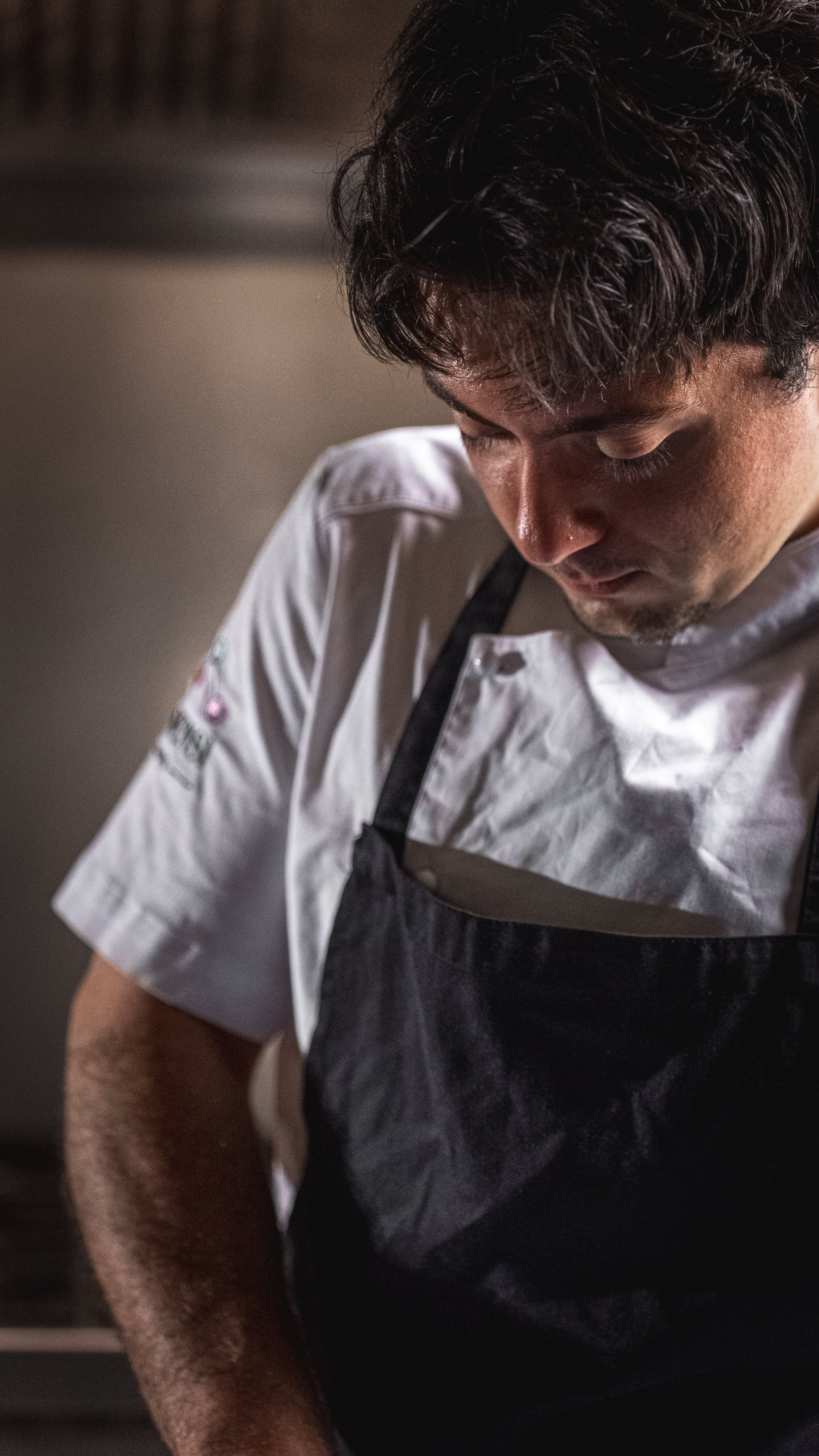 Un uomo in divisa da chef che si concentra mentre lavora, con sfondo sfocato.