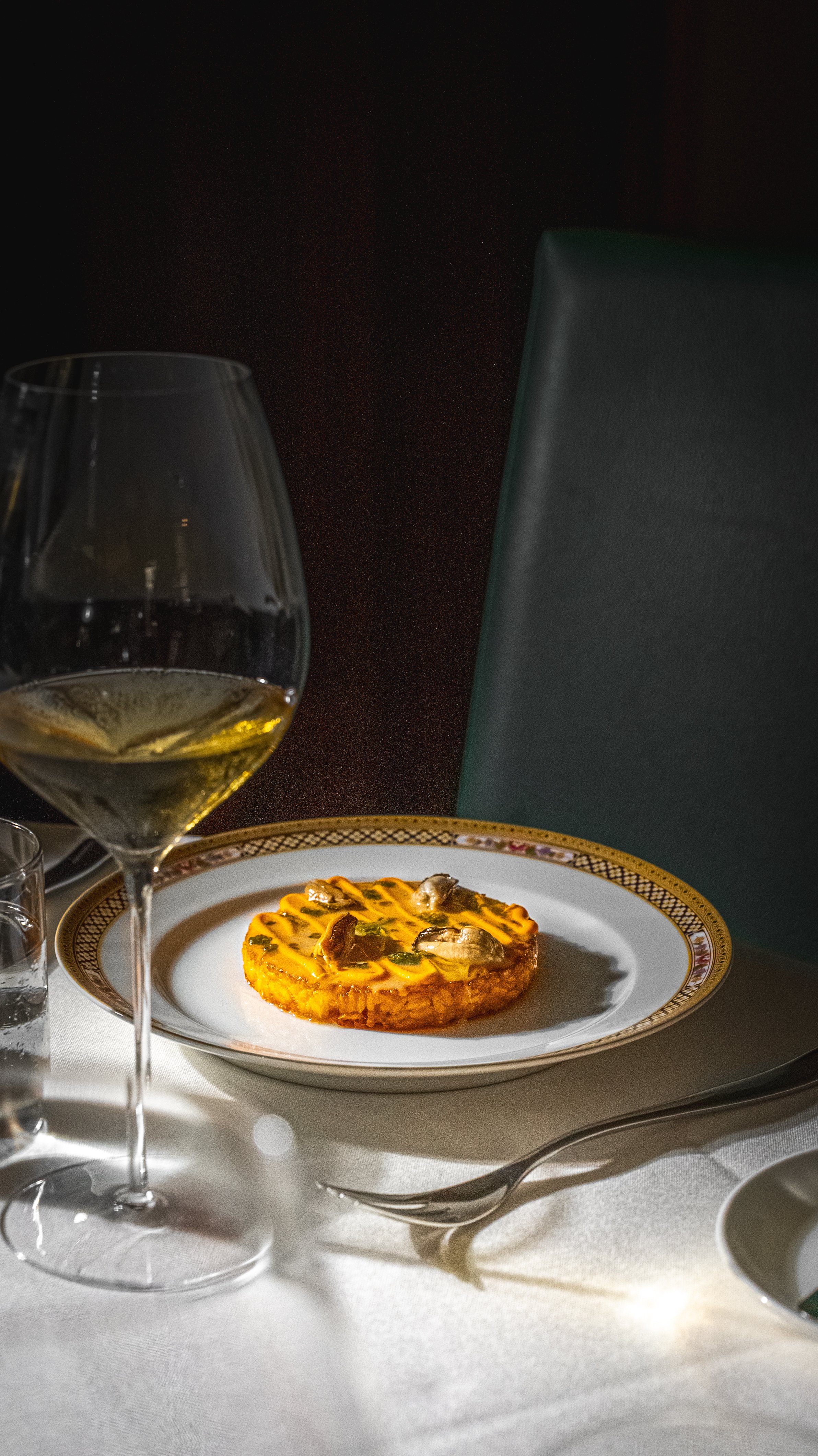 Un bicchiere di vino bianco e un piatto con una tartina con funghi, formaggio e verdure, su un tavolo apparecchiato elegantemente.