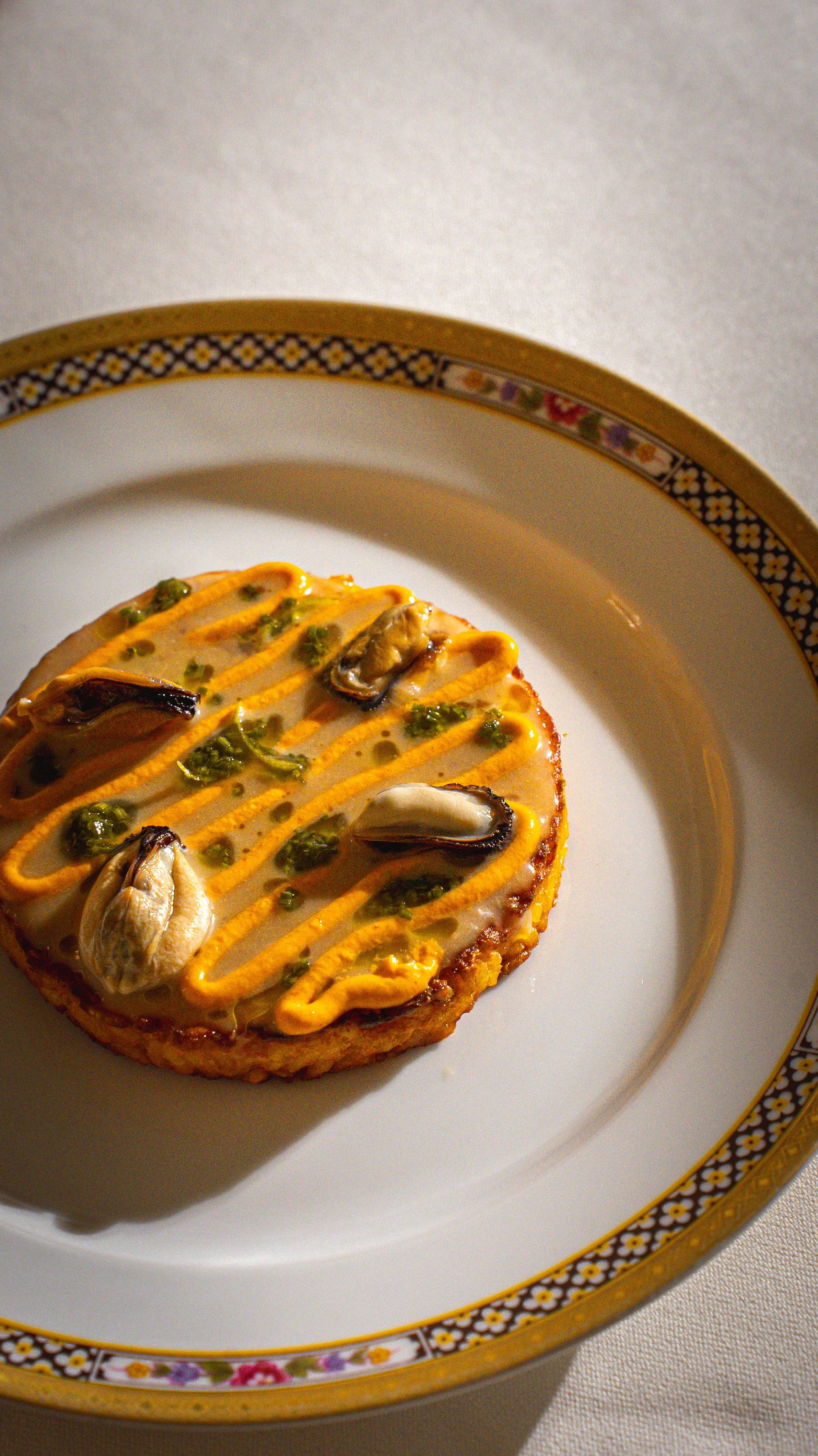 Tarte salata con cozze, decorata con maionese all'aglio e prezzemolo, su un piatto decorato con bordi floreali.