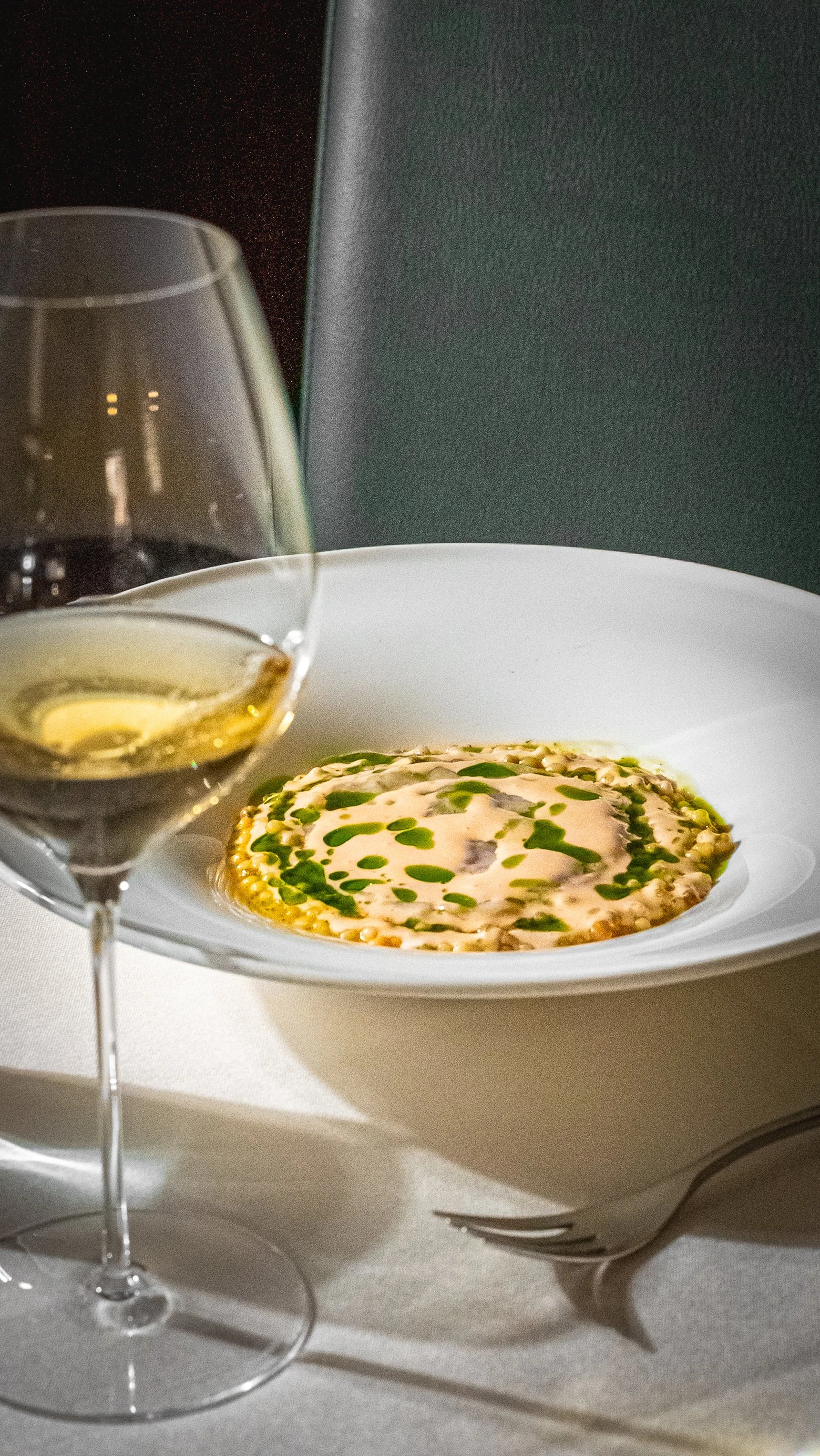 Calamaro ripieno su piatto bianco con olio e prezzemolo affianco. Bicchiere di vino bianco in primo piano.
