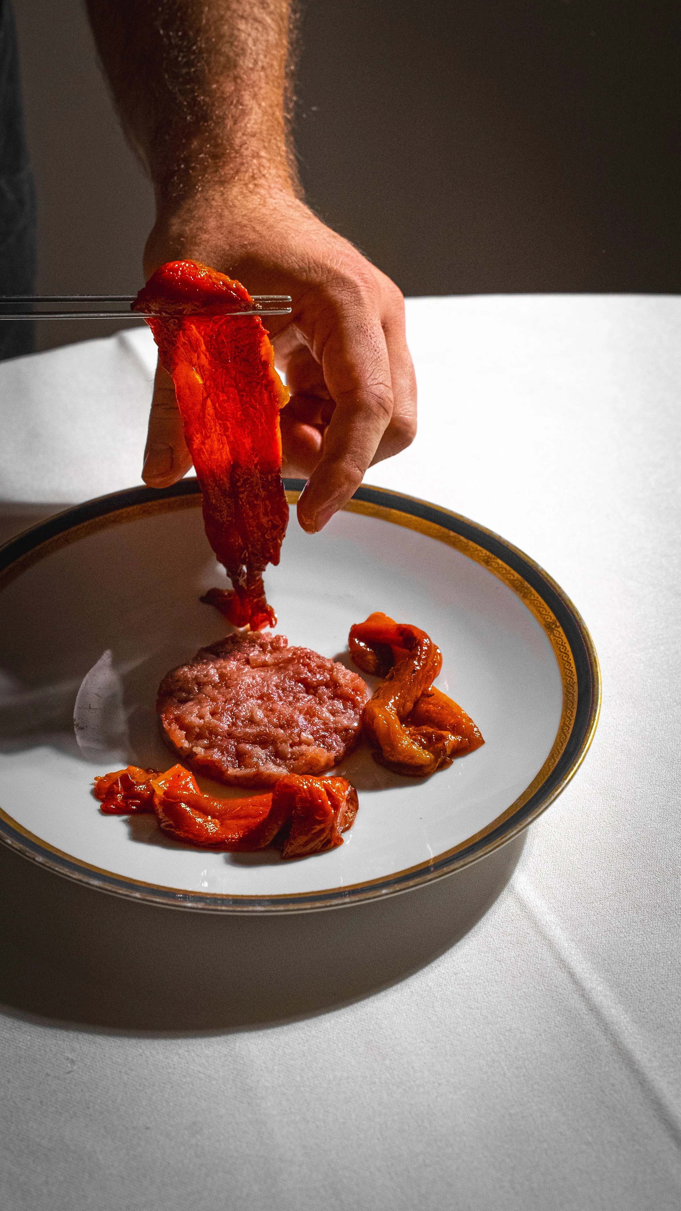 Preparazione di carne e peperoni su un piatto con un coltello a punta, ambientato in un contesto di cucina o sala da pranzo.